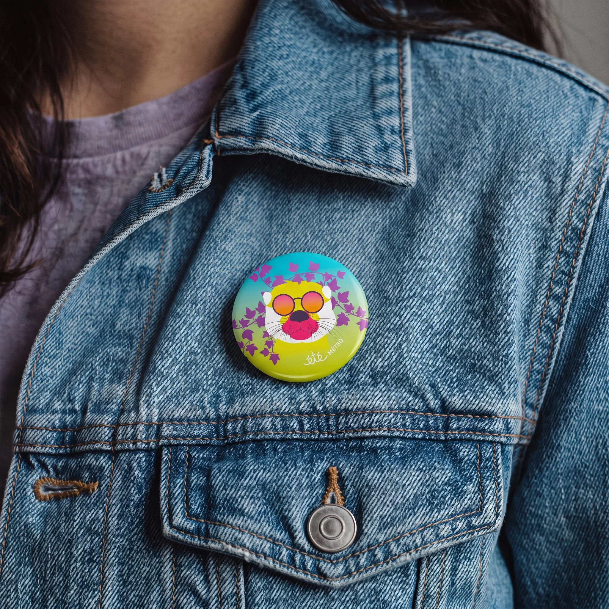 Veste en jean bleu avec des coutures orange, portant un badge rond coloré avec un lion stylisé et des feuilles violettes, porté avec un t-shirt violet clair.