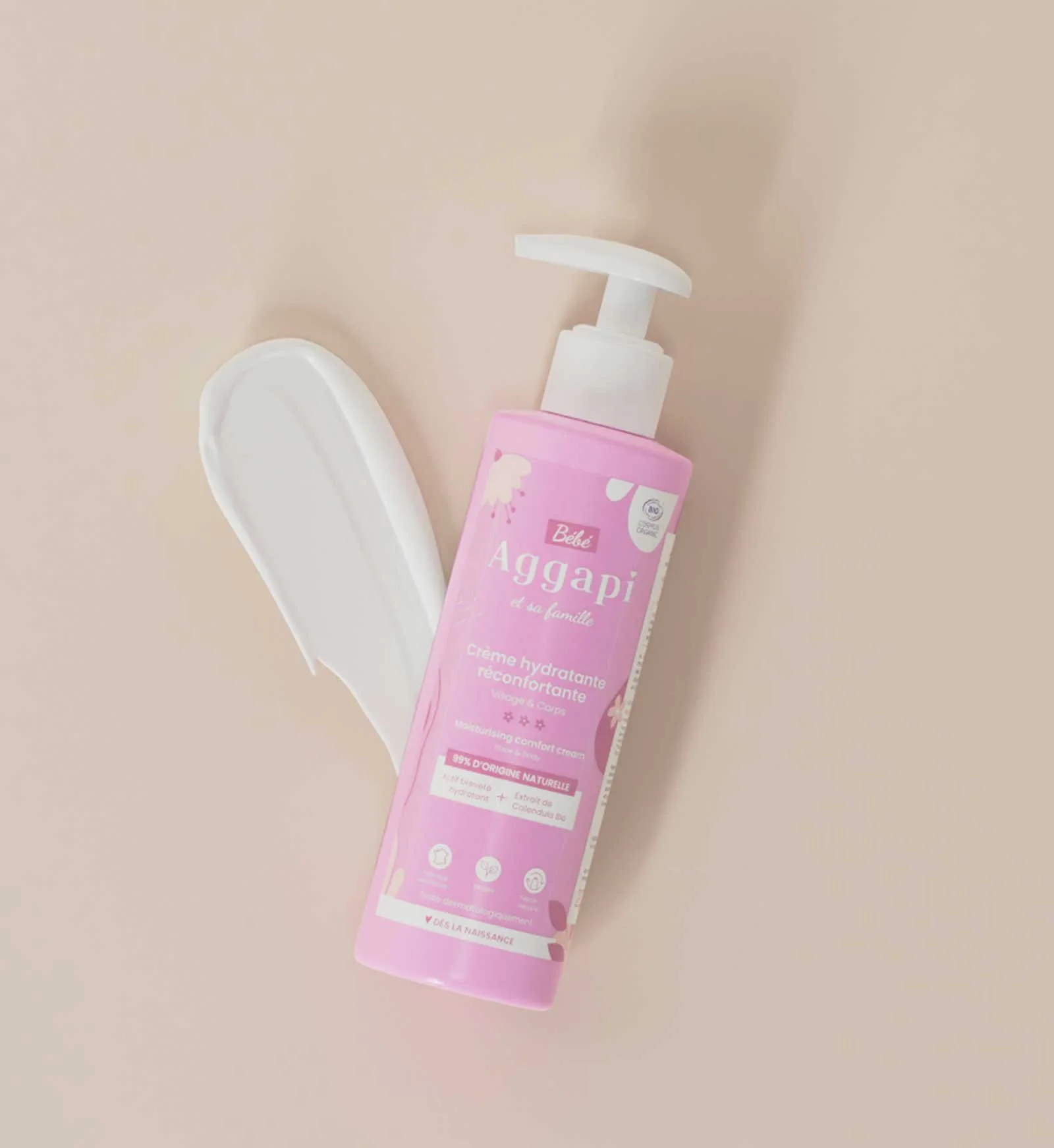 Bouteille de crème hydratante pour bébés de couleur rose avec un distributeur blanc, placé sur un fond beige. La bouteille est de marque Agapi, recommandée pour le visage et le corps.