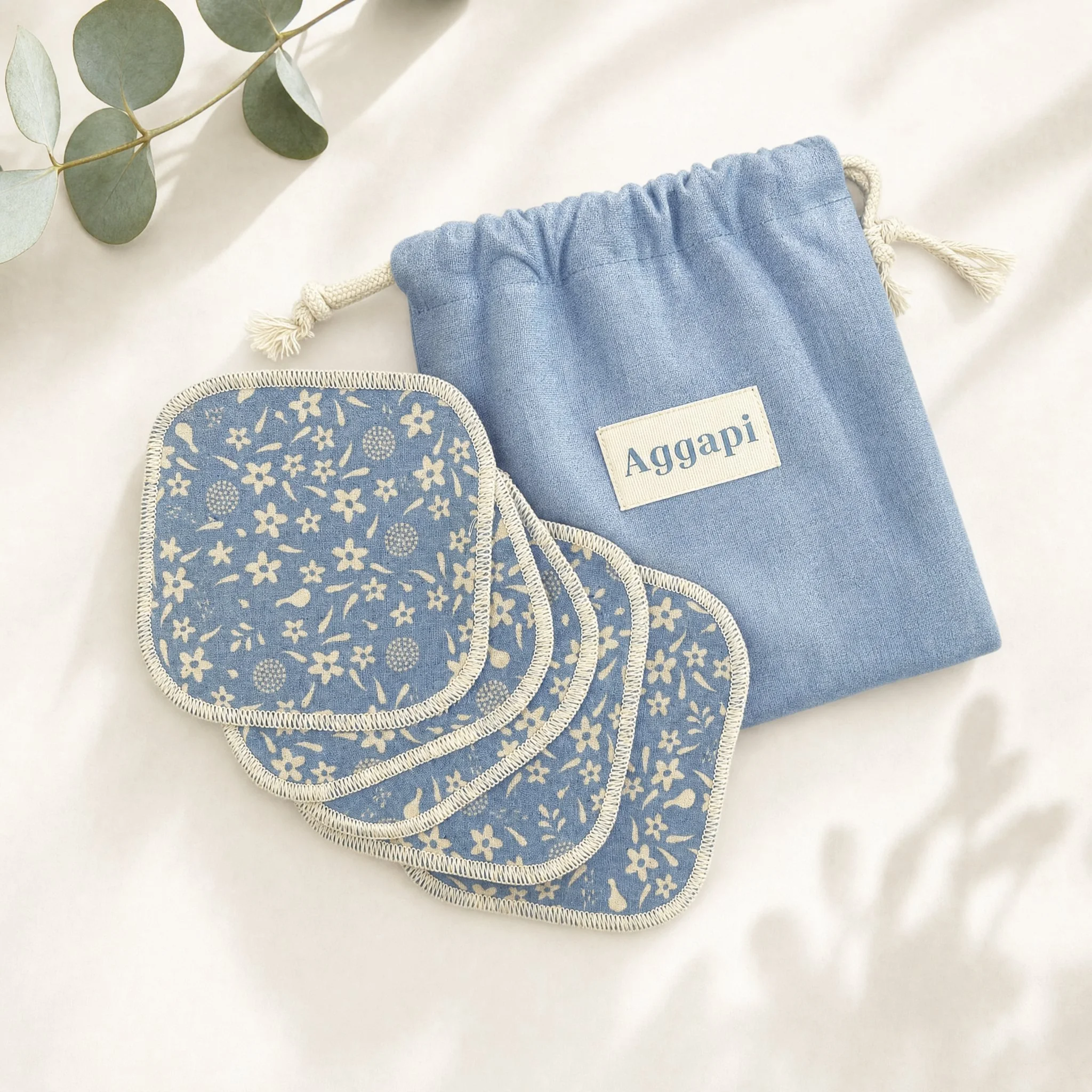 Petites pochettes en tissu avec motifs floraux, une en bleu avec un dessin floral blanc, une autre en bleu avec un fond uni, et une en tissu eucalyptus à gauche, décoratives, sur un fond blanc.