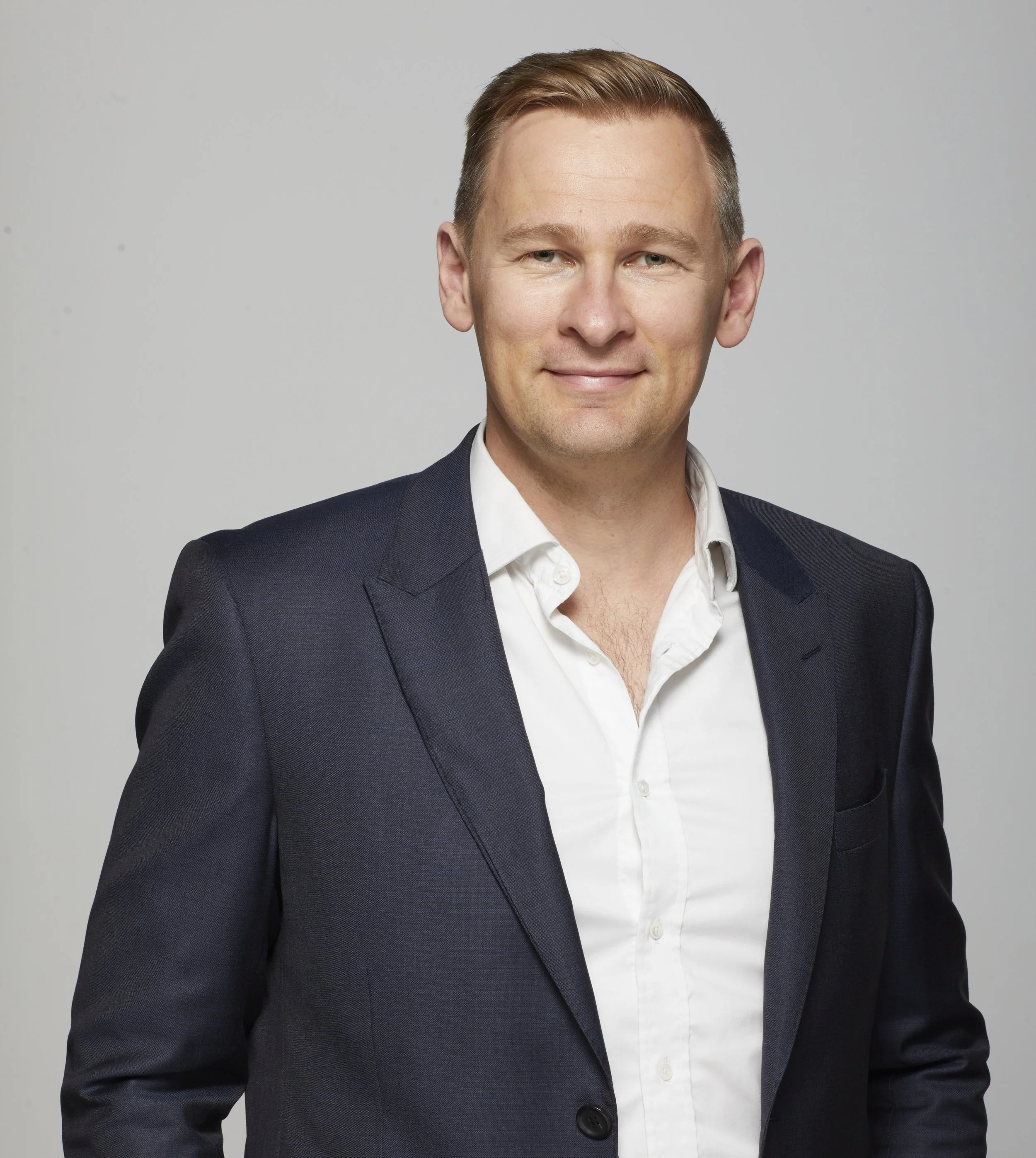 Headshot of Peter Forster in a dark suit and white shirt, smiling against a plain gray background.