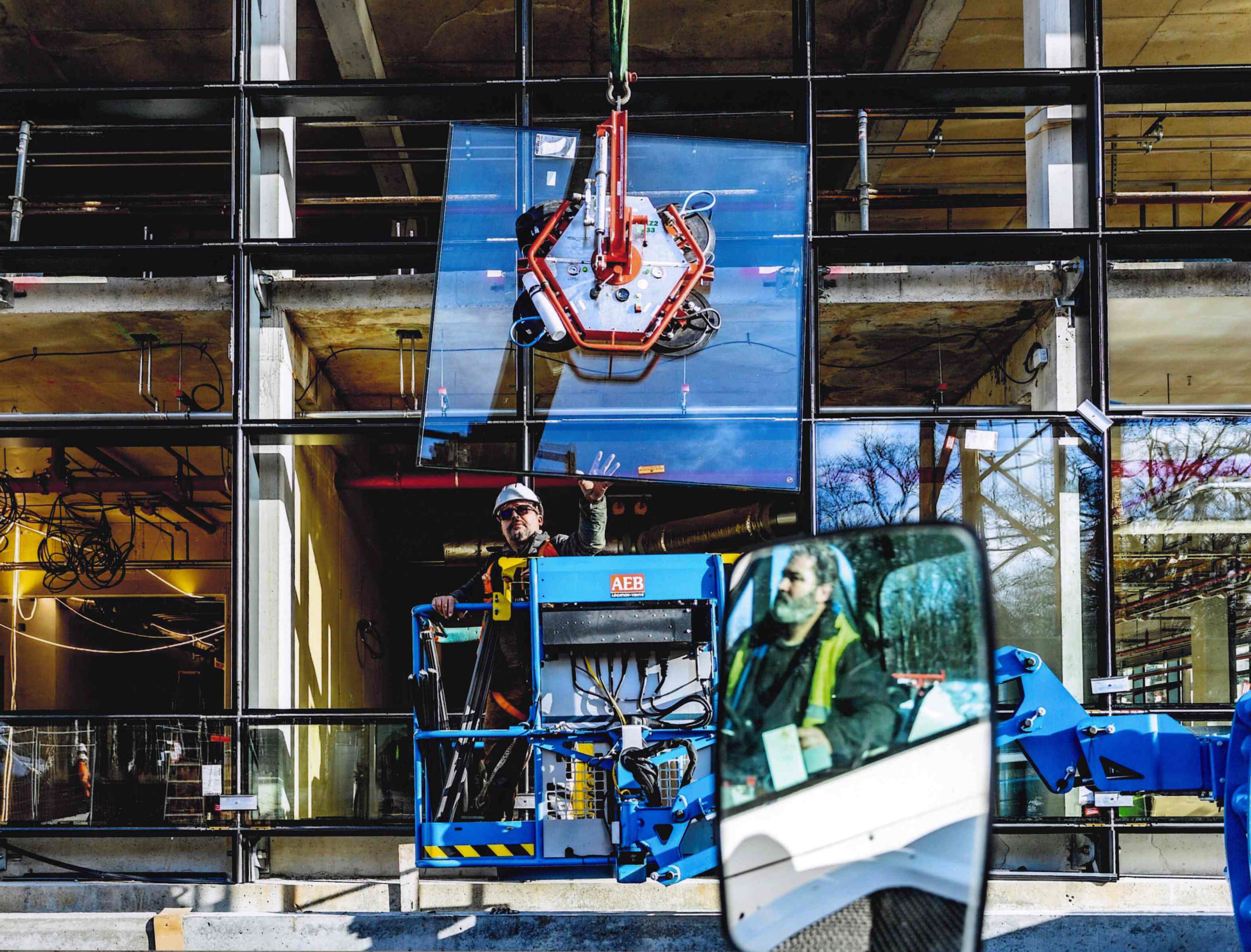 Des ouvriers utilisent un chariot élévateur pour effectuer des travaux dans la façade en verre d'un immeuble en construction.