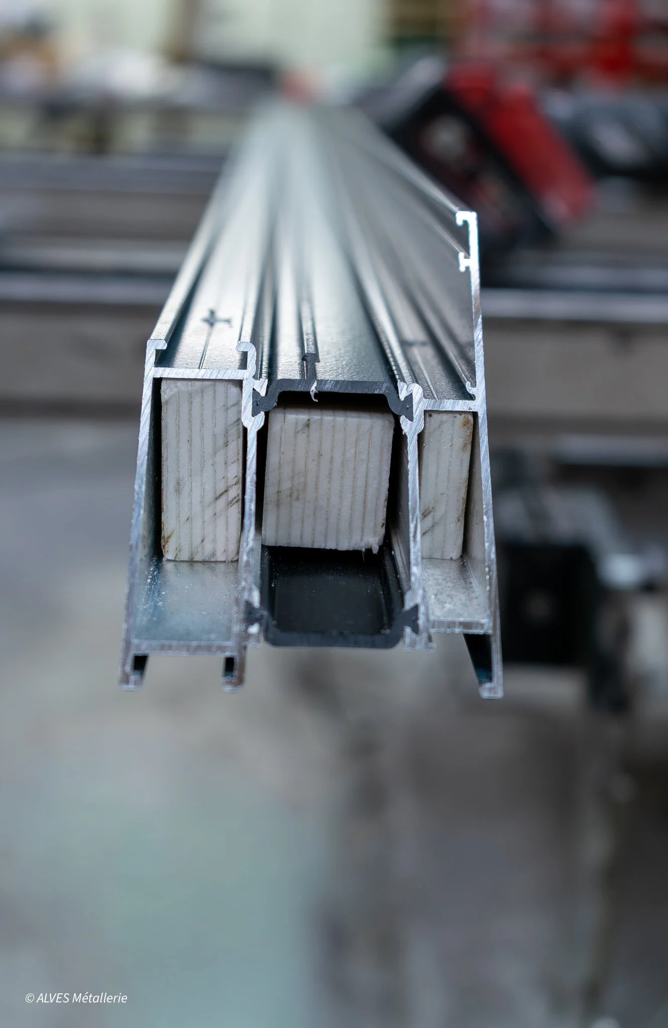 Un profilé en aluminium avec un système de fixation, destiné à la fabrication de fenêtres ou portes, posé sur une surface dans un environnement industriel.