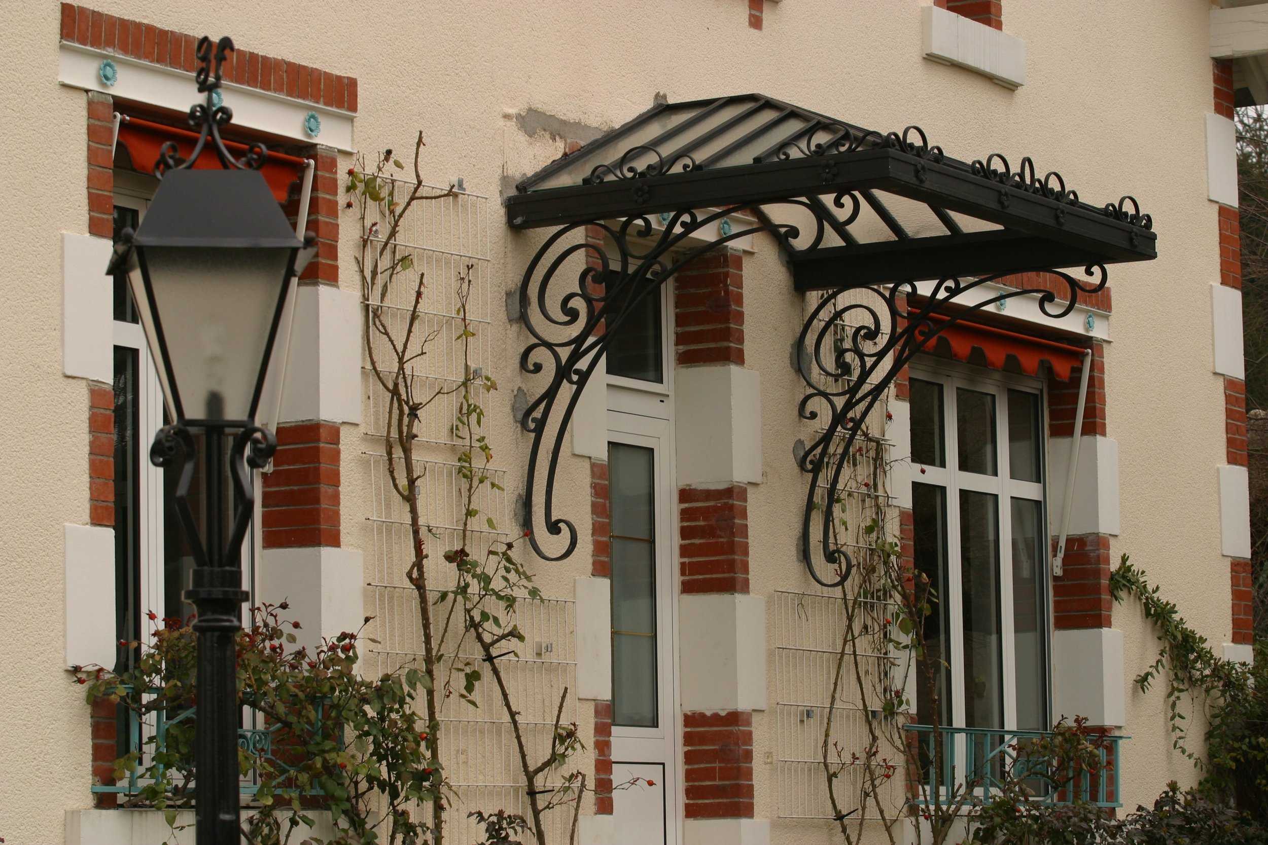 Façade d'un bâtiment résidentiel avec fenêtres, fleurs décoratives, porte d'entrée, et un lampadaire noir devant.