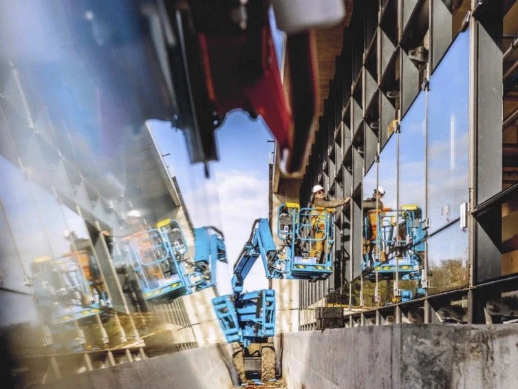 Travaux de construction avec deux opérateurs sur une plateforme élévatrice face à un bâtiment en rénovation.