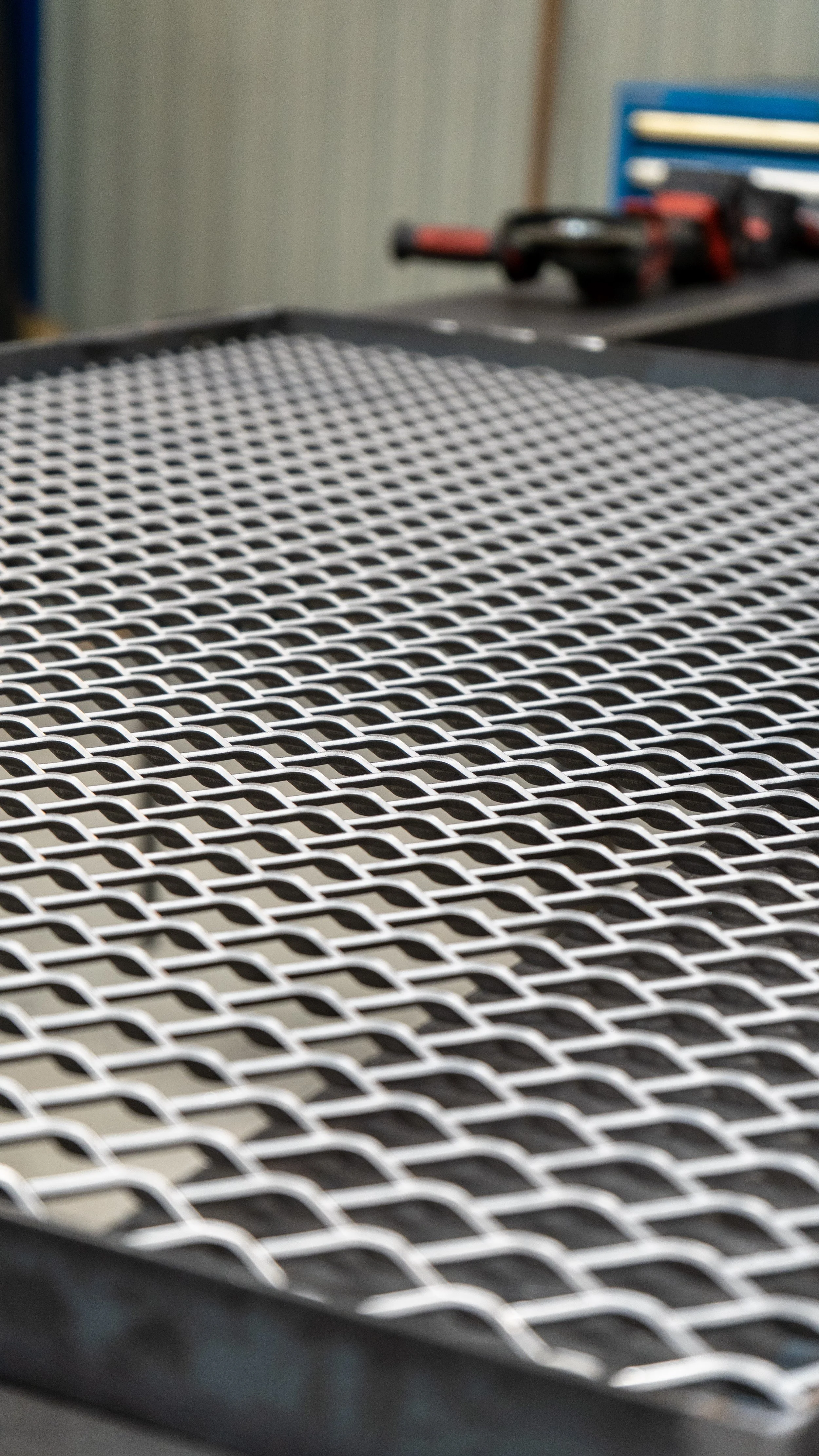 Grille métallique de forme rectangulaire sur une surface sombre avec des outils en arrière-plan dans un atelier.