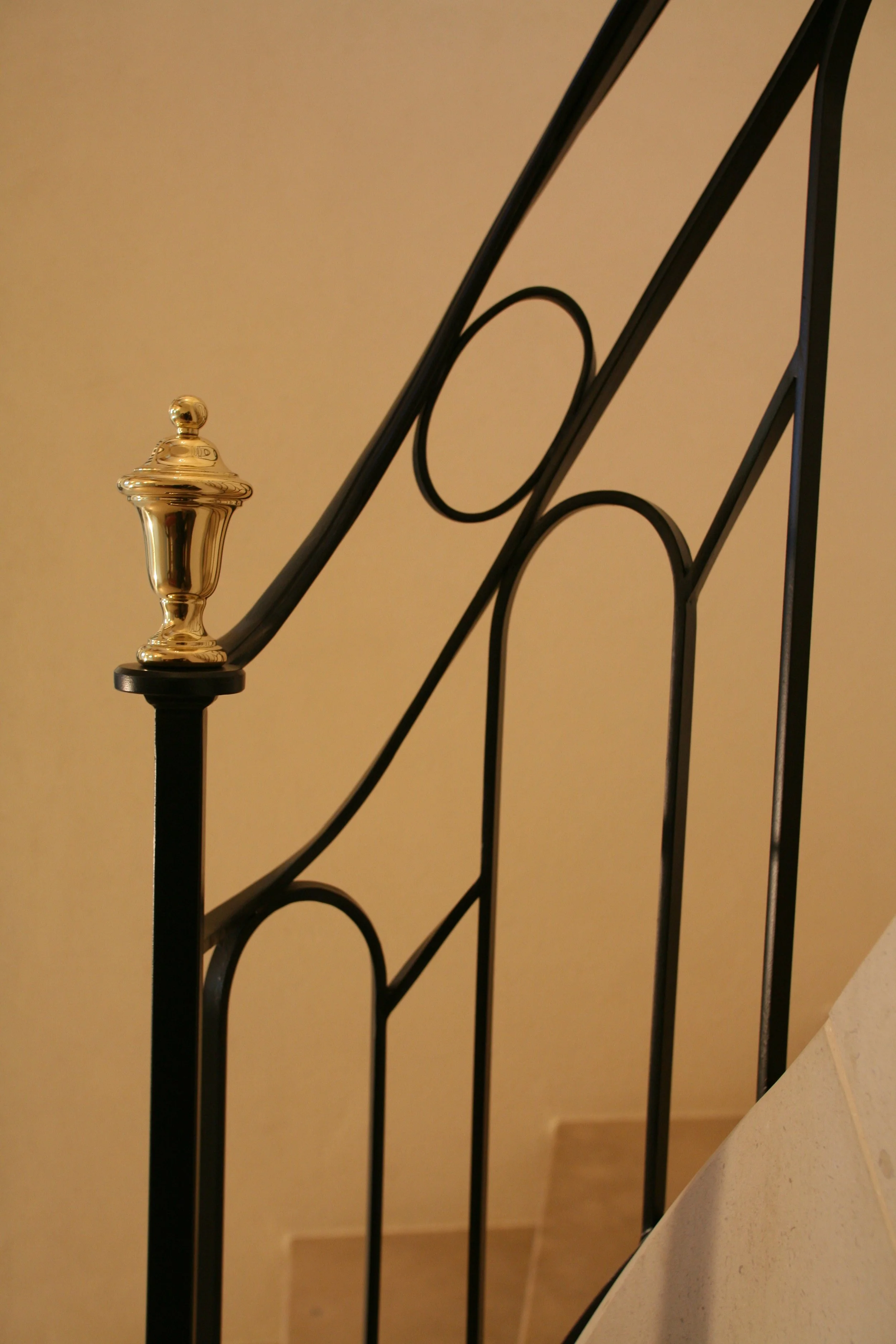 Une rampe d'escalier en métal noir avec un élément décoratif en forme de cloche en or à la tête de la barrière.