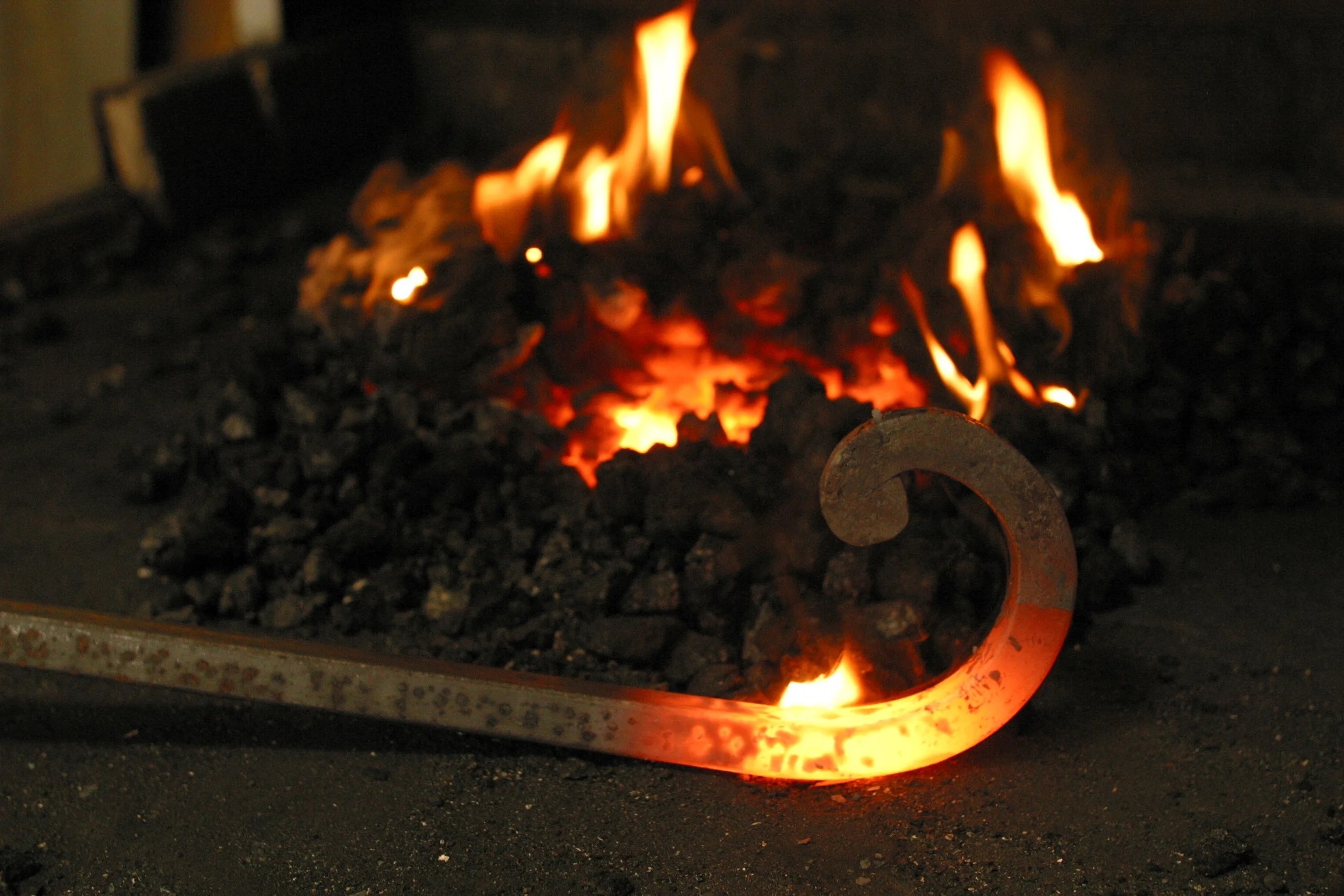 Un foyer de forge avec des braises chaudes et des flammes orange, utilisant une loupe pour manipuler le métal en fusion.