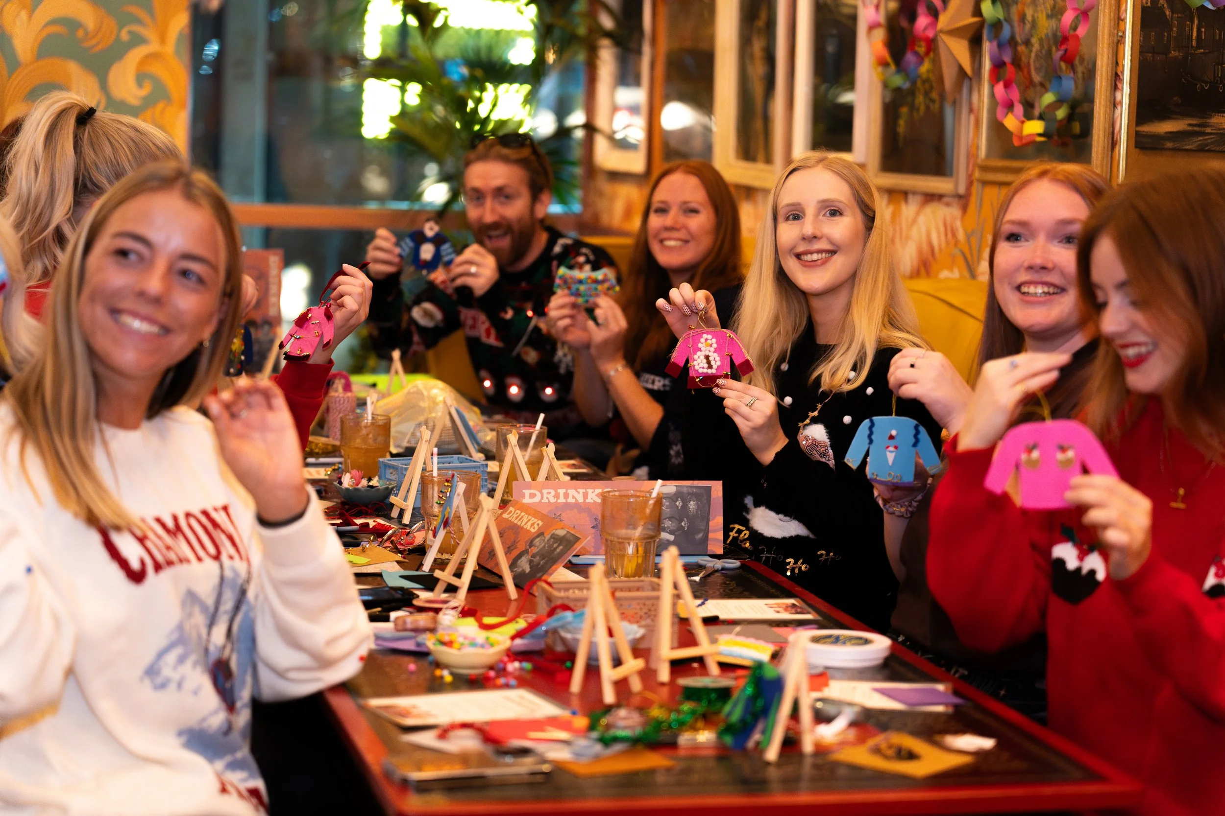 PeopleEnjoyingFestiveHolidayDecorationsAndArtsAndCrafts at a gathering, with smiles and holiday-themed crafts.