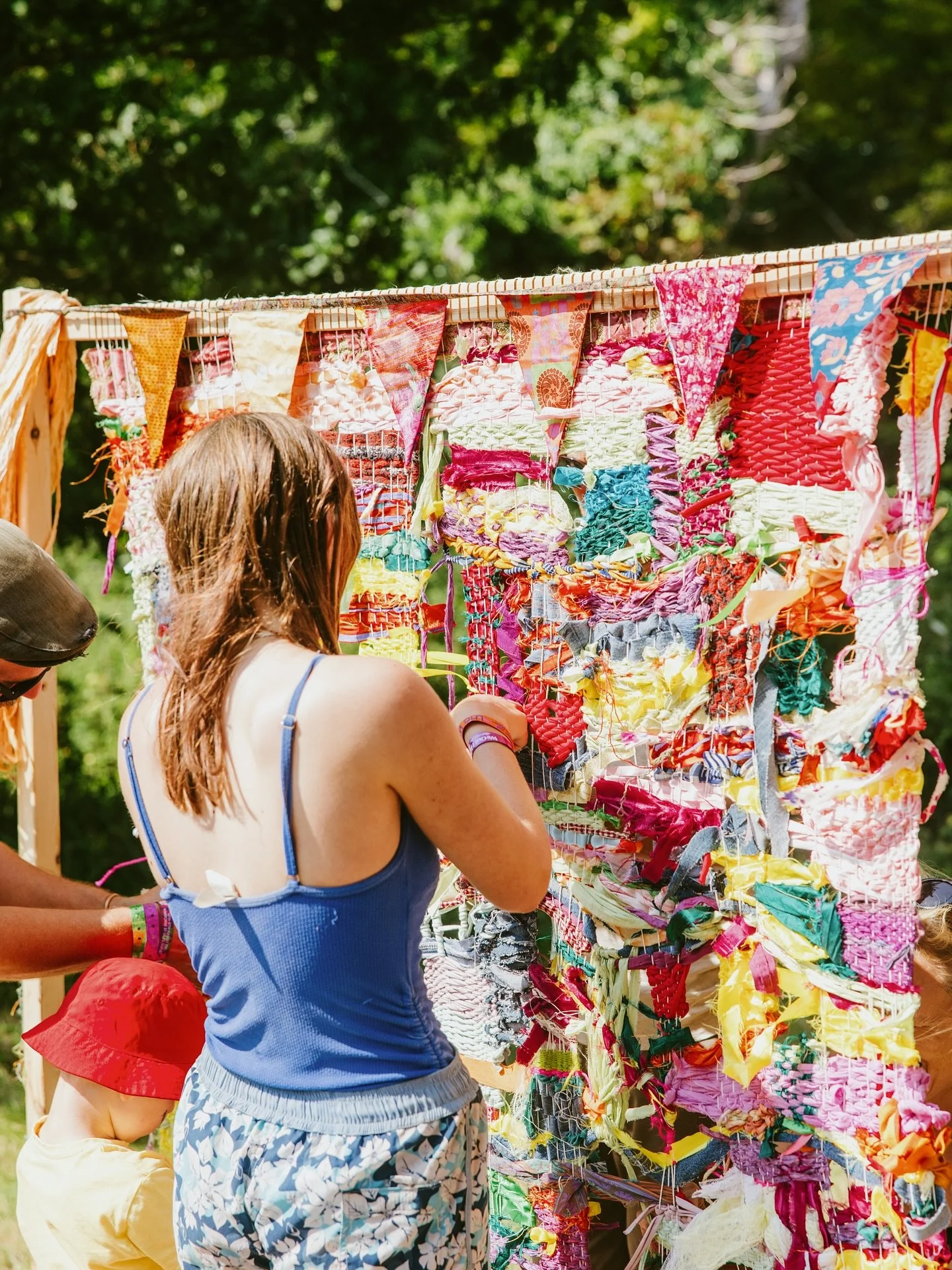 People browsing a colorful textile or craft stall at an outdoor event.
