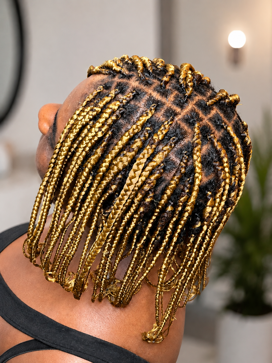 Close-up of a person's head showing freshly done braids with black roots and gold-colored extensions.
