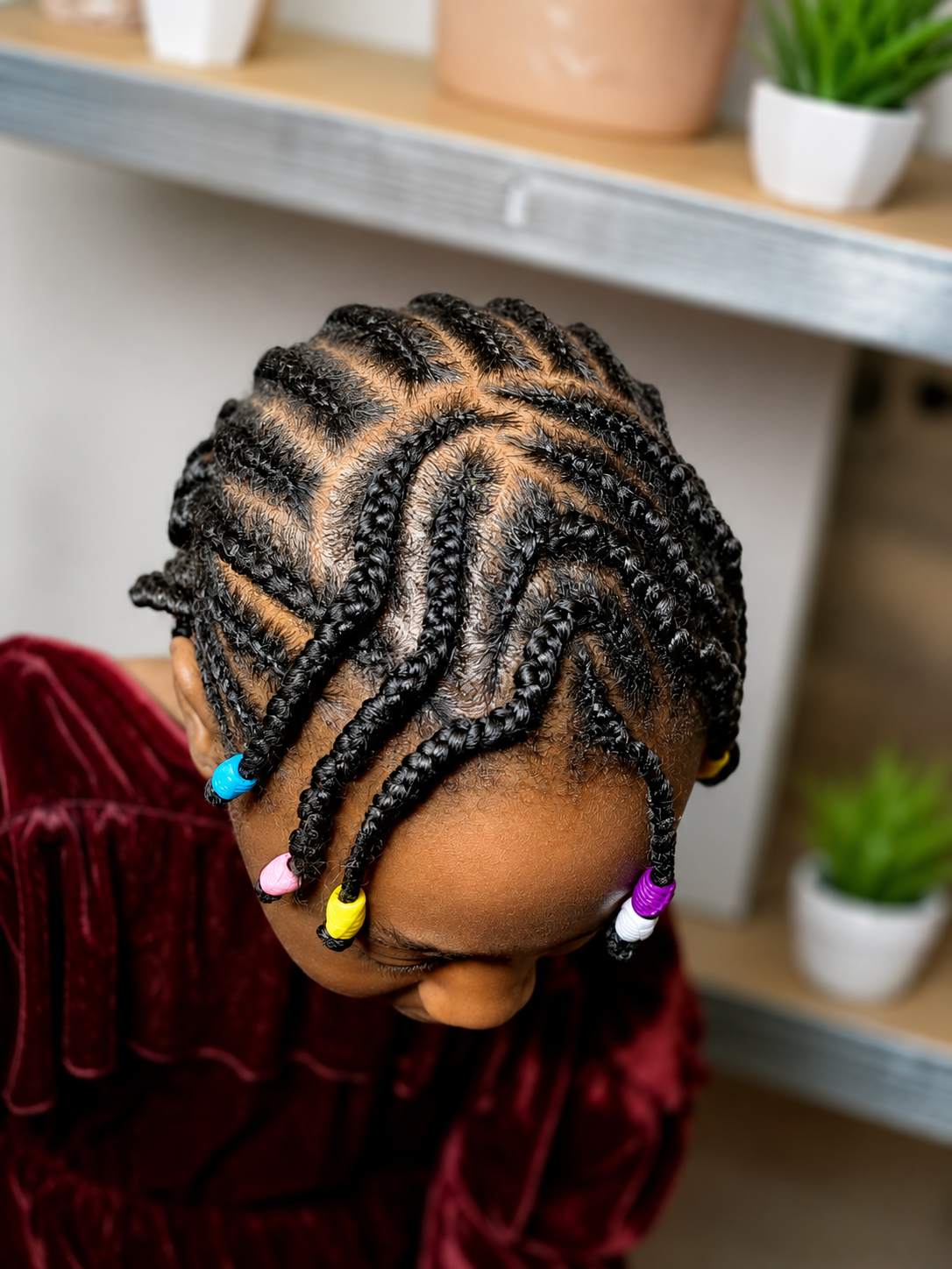Close-up of a child's head with neatly done box braids decorated with colorful beads.