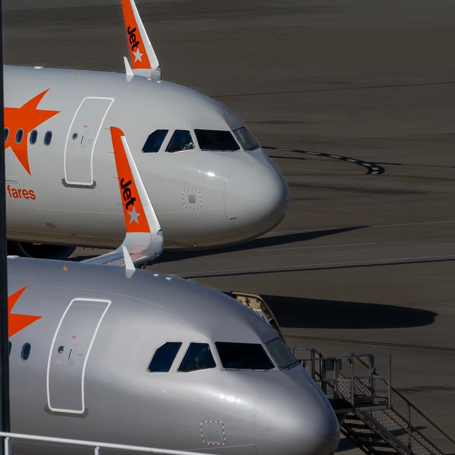 Close-up of the front sections of two JetBlue airplanes parked at an airport gate, with connecting jet bridges and ground support equipment visible.