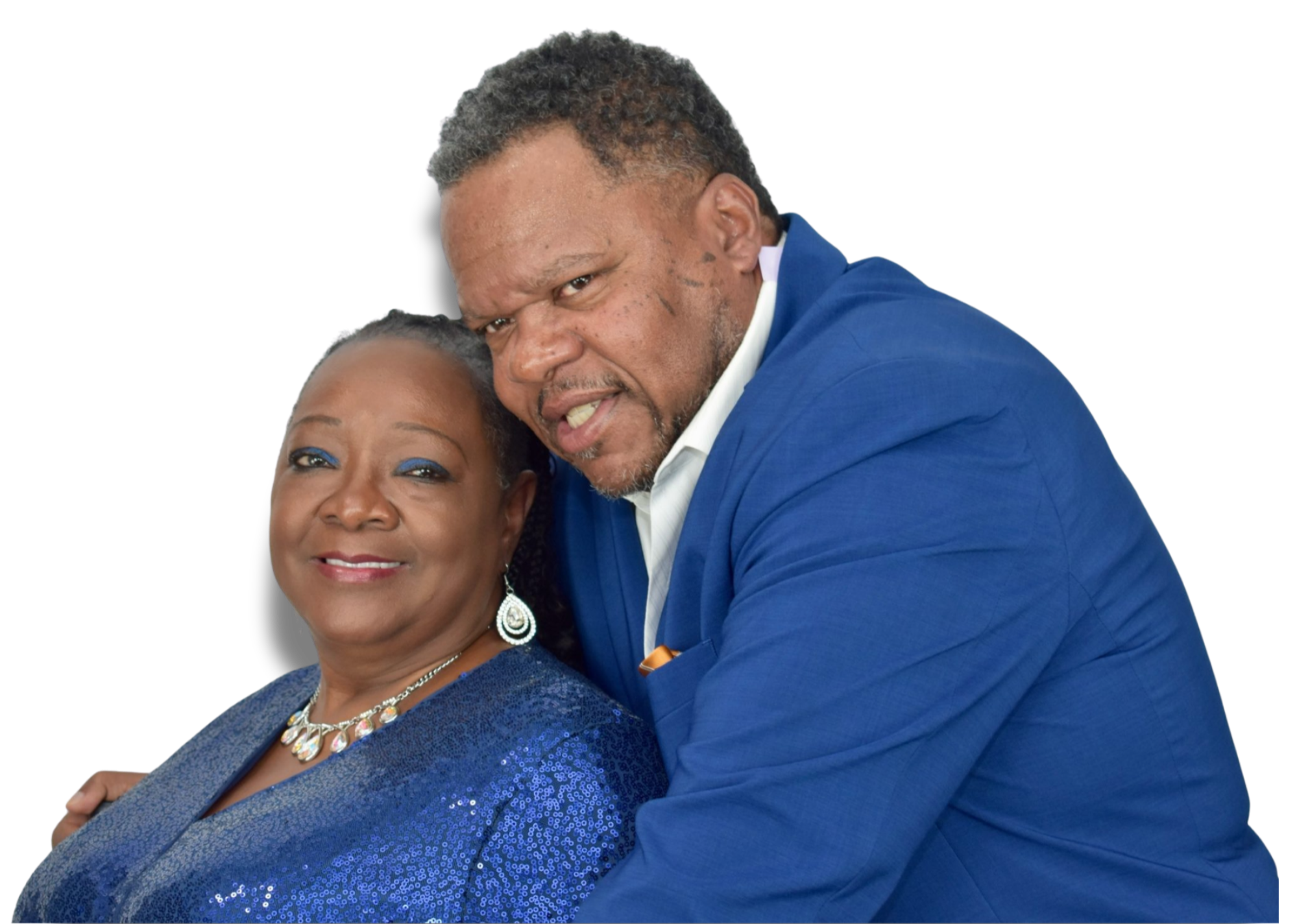 A man and a woman are posing closely together, both dressed in blue. The woman is smiling and wearing a blue sequin dress with matching earrings, and the man is leaning his face close to hers, smiling, wearing a blue suit.