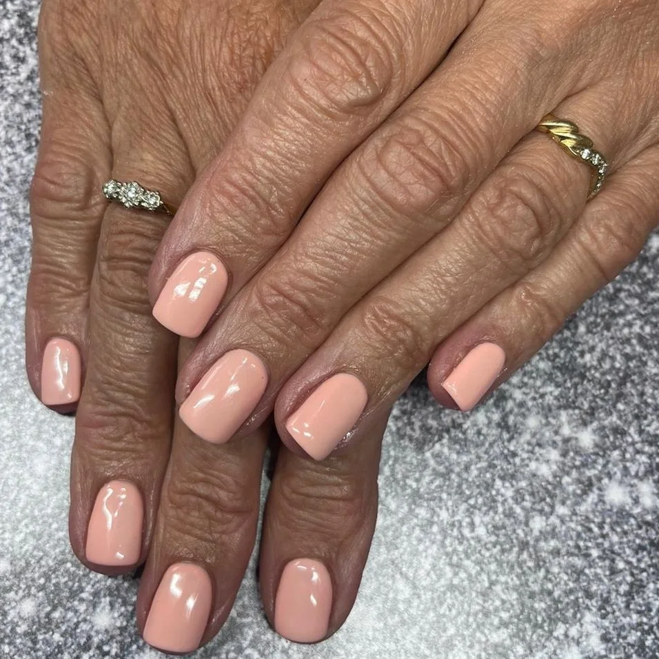 Close-up of two hands with natural skin, showing freshly manicured nails painted in soft pink, adorned with wedding and engagement rings on the ring fingers.