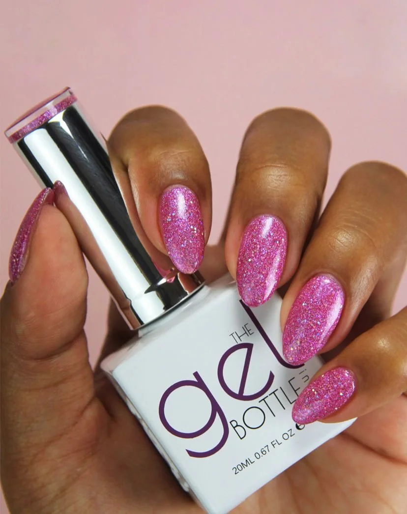 Hand holding a small white bottle of nail polish with pink glittery nails painted on fingernails.