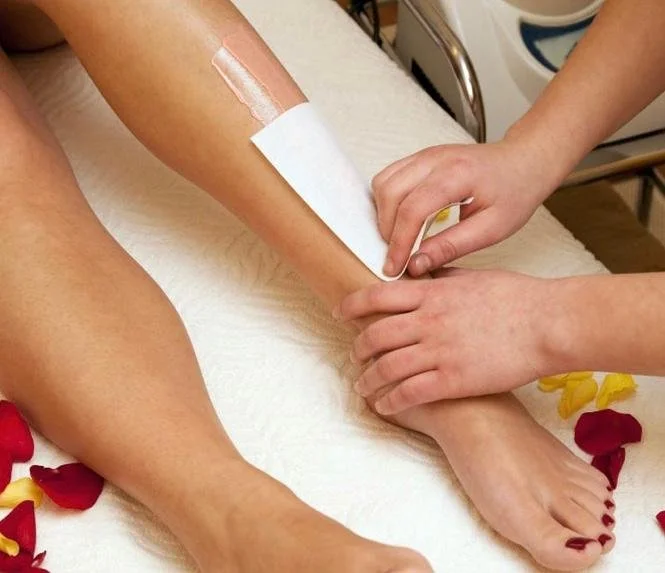 Person receiving a medical treatment involving a bandage on their lower leg, with another individual applying it while lying on a white bed with red and yellow flower petals.
