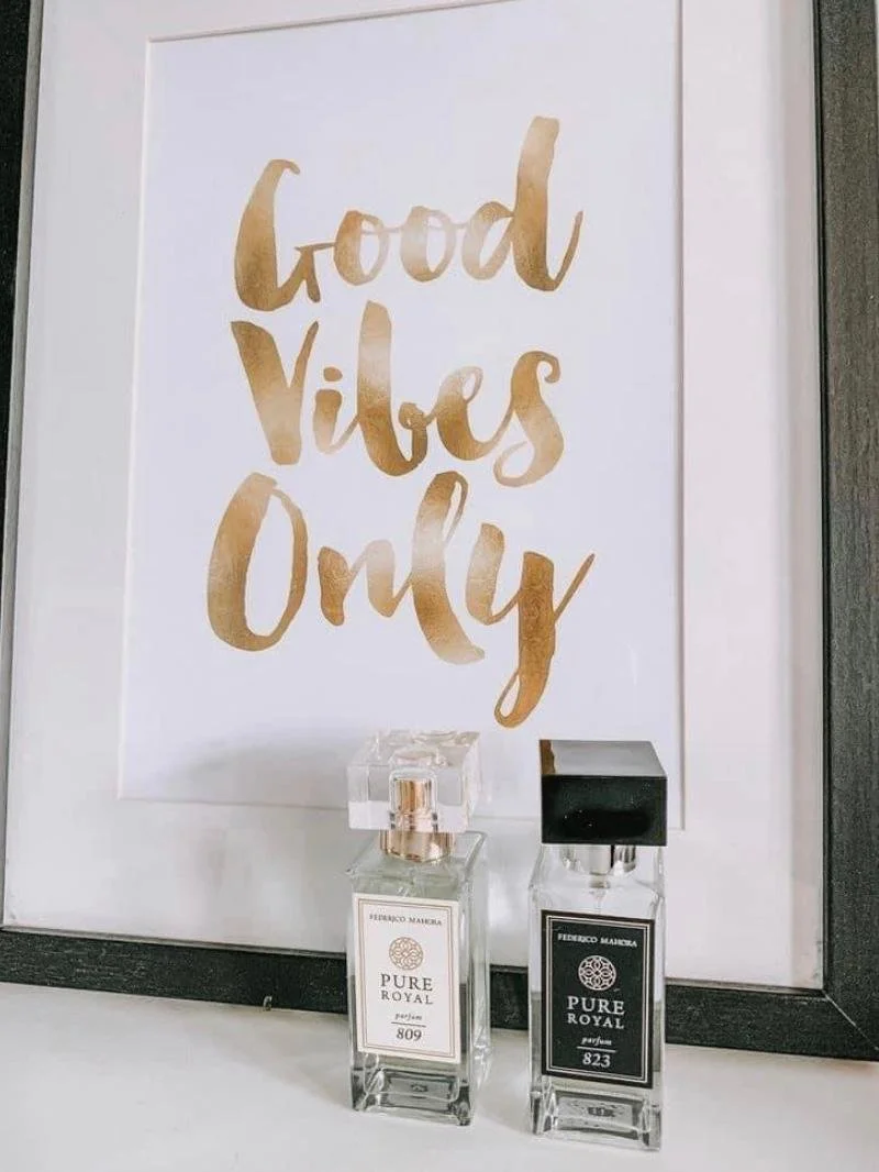 A framed sign with gold cursive text reading 'Good Vibes Only' and two bottles of perfume placed in front.
