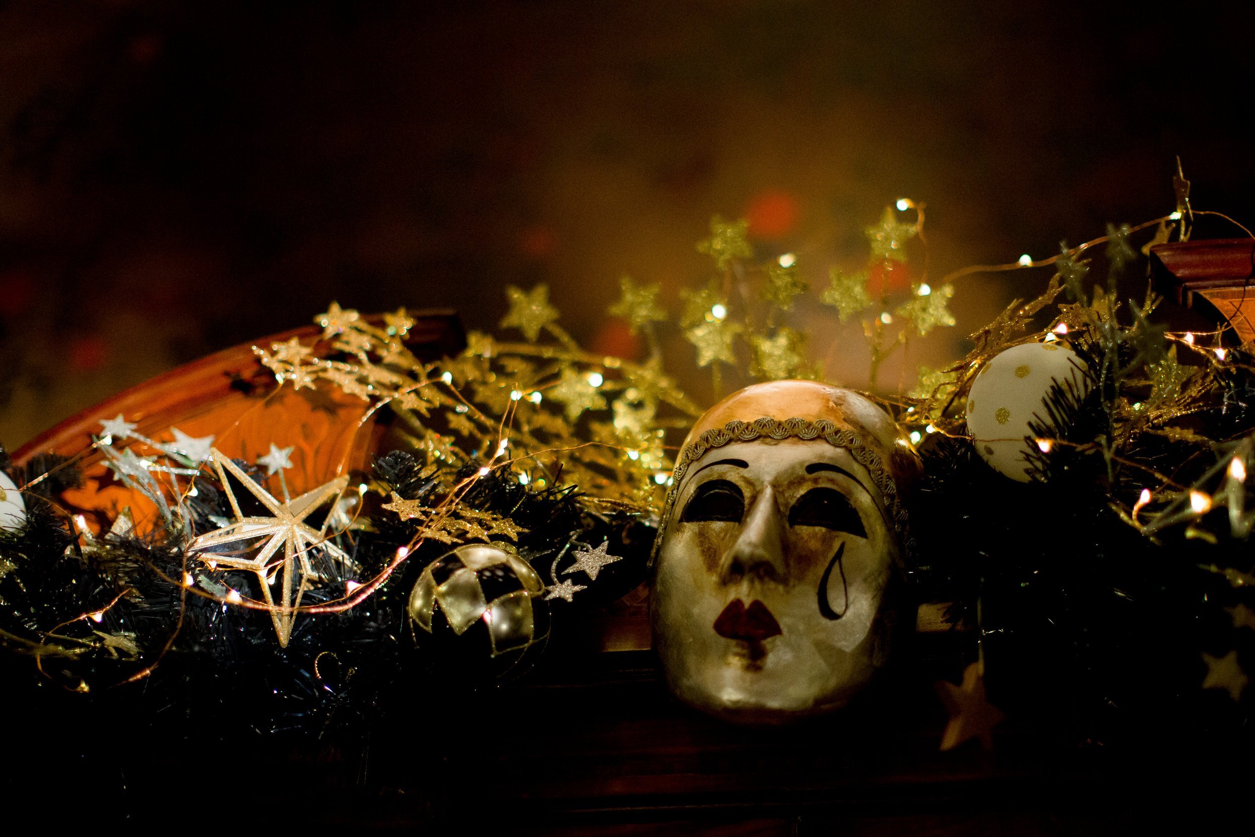 A decorative arrangement with a skull mask, holiday lights, ornaments, and gold star decorations on a dark background.