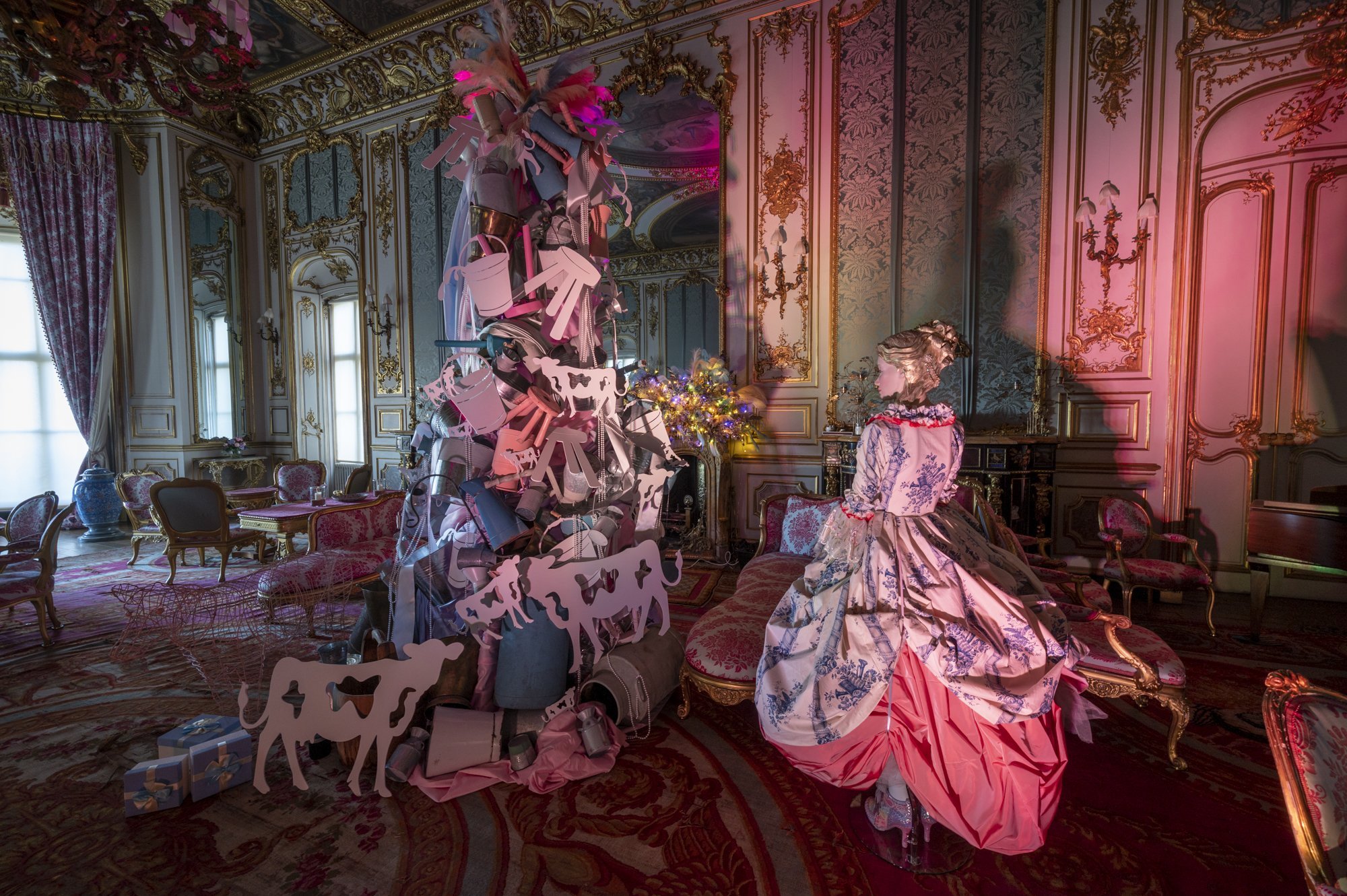 An ornate room with pink and gold decor, featuring a mannequin dressed in an elaborate gown, and a Christmas tree decorated with pink and white paper animal cutouts and lights.