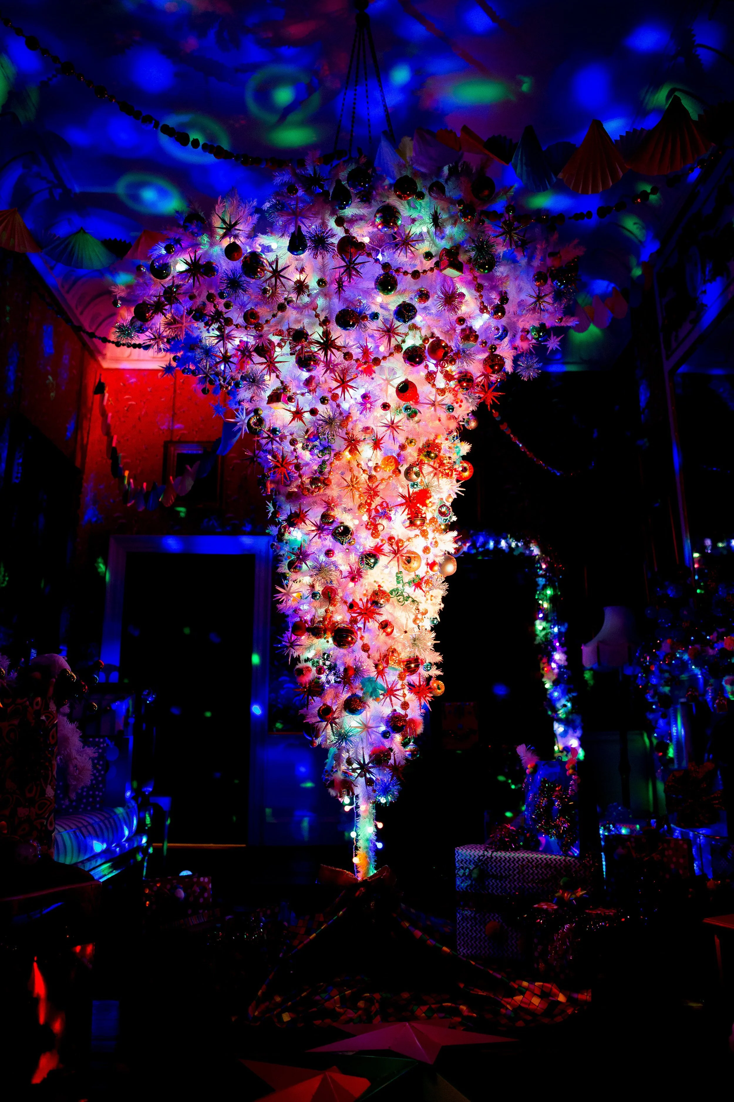 Colorful Christmas tree with ornaments and decorations, lit with vibrant multicolored lights in a dark room.