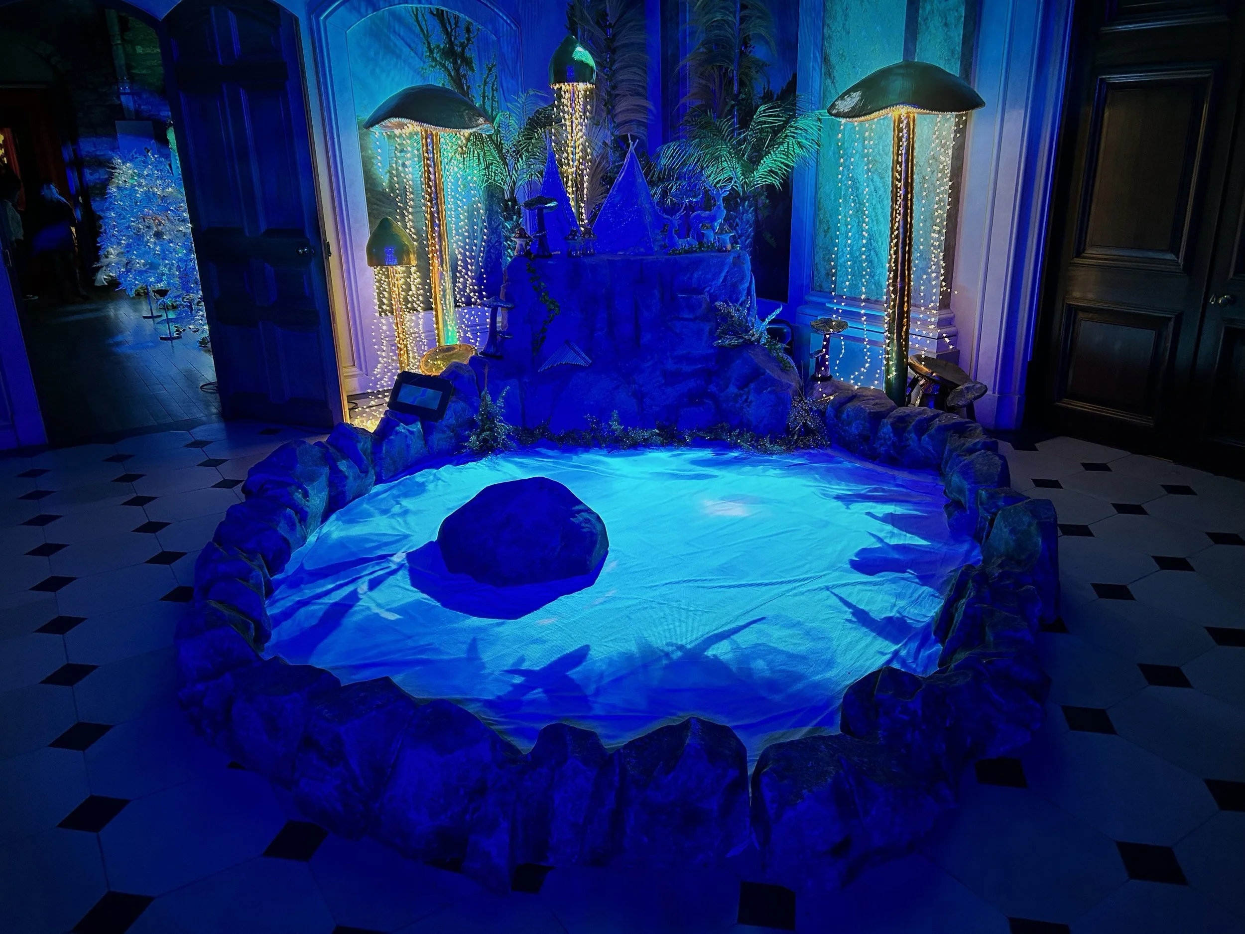 A display of decorative glowing mushrooms and plants with a blue and green color scheme, set on a rocky base in an indoor setting.