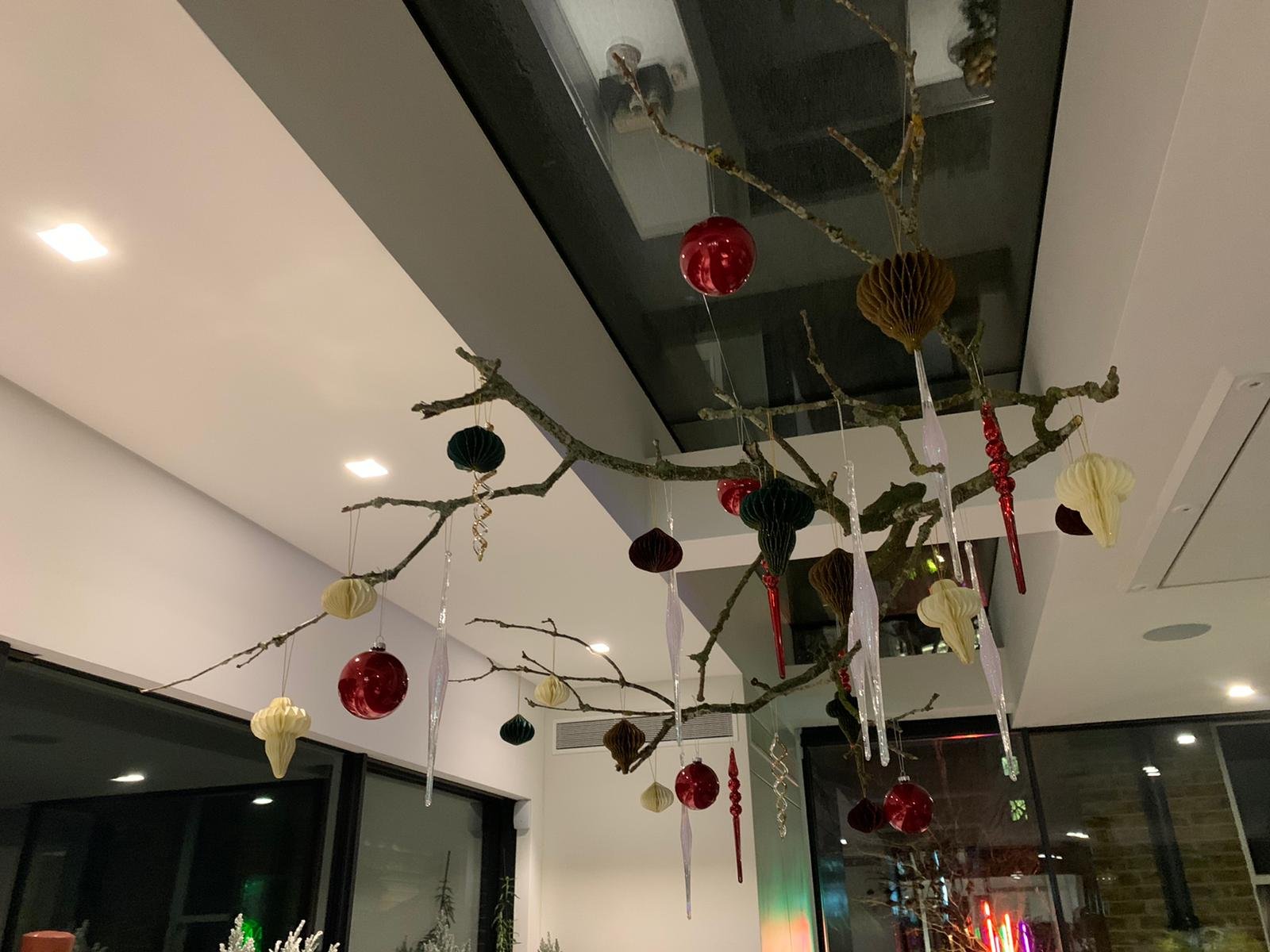 Decorative branch hanging from ceiling with red, black, and cream ornaments and icicle decorations in an indoor setting.