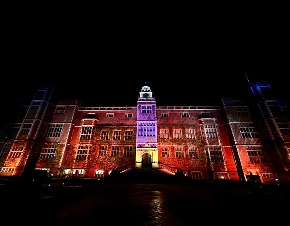 A large historic brick building illuminated with colorful lights outdoors at night.