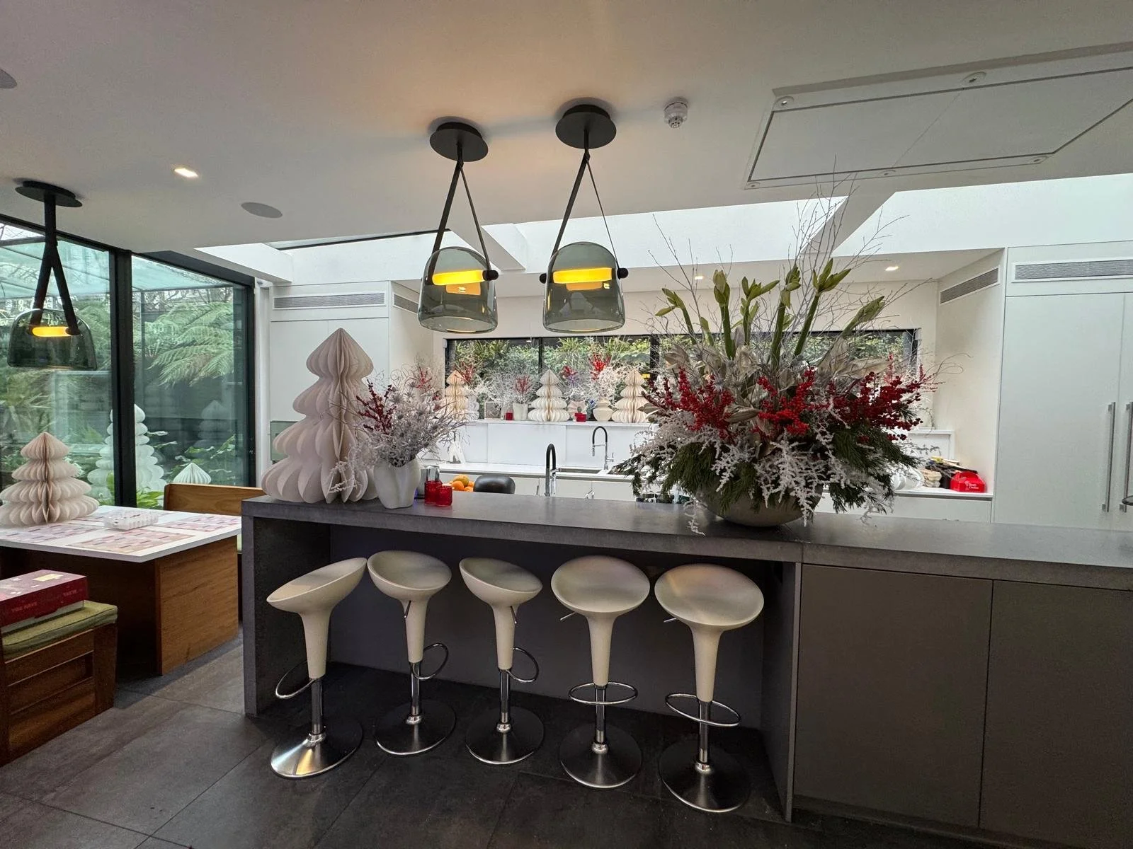 Modern kitchen with white cabinets, large window, floral arrangements, and barstools at a kitchen island.