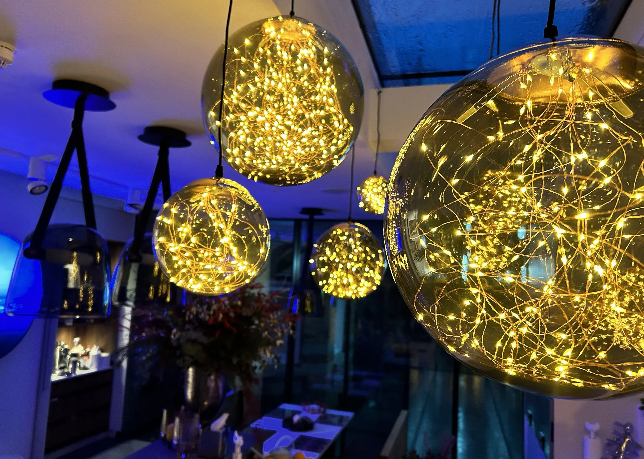 Multiple spherical glass pendant lights with intricate gold wire designs illuminated with warm yellow LED lights hanging in a modern interior space.
