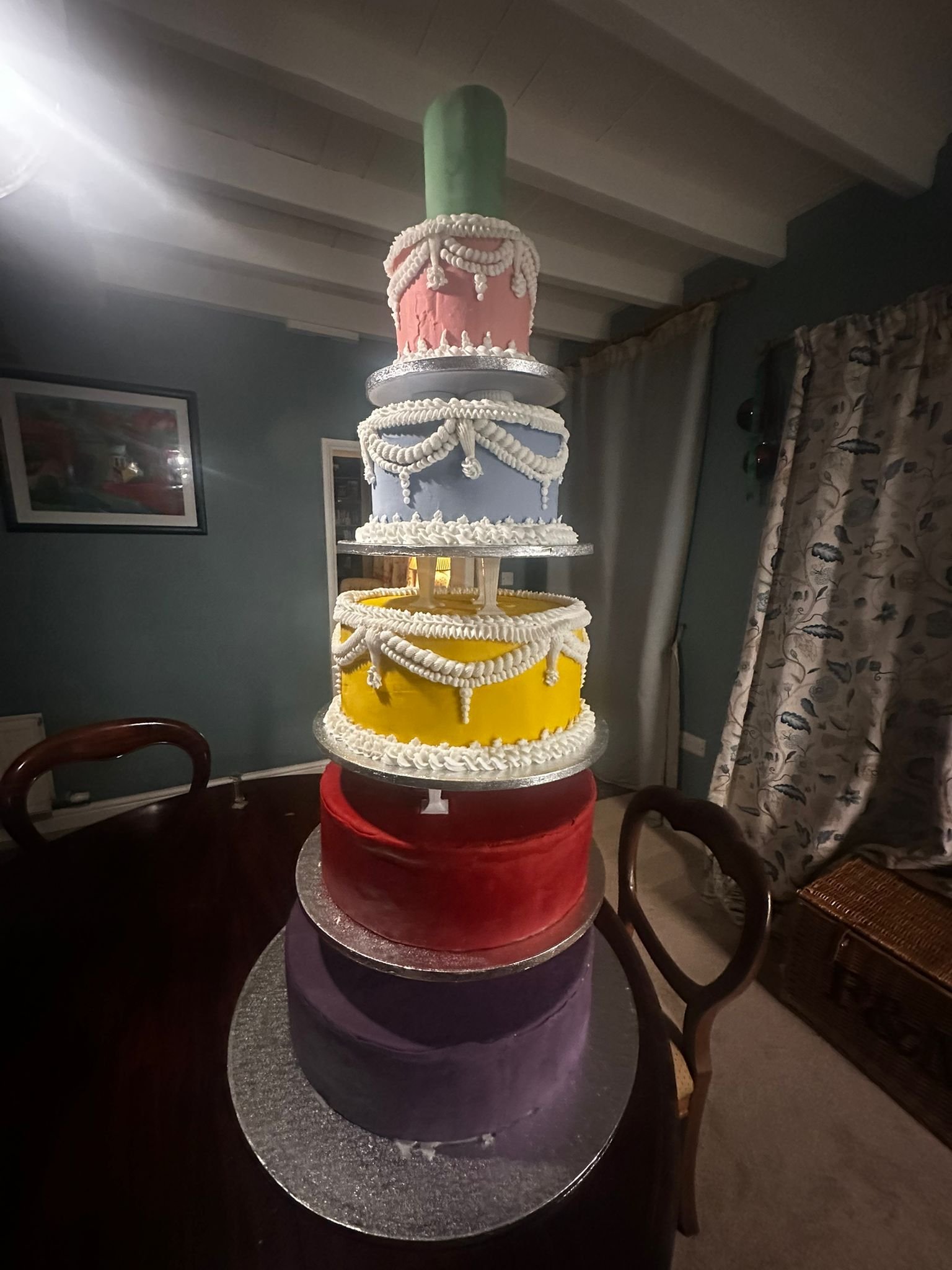 A five-tiered birthday cake with colorful decorated tiers, topped with a green candle.