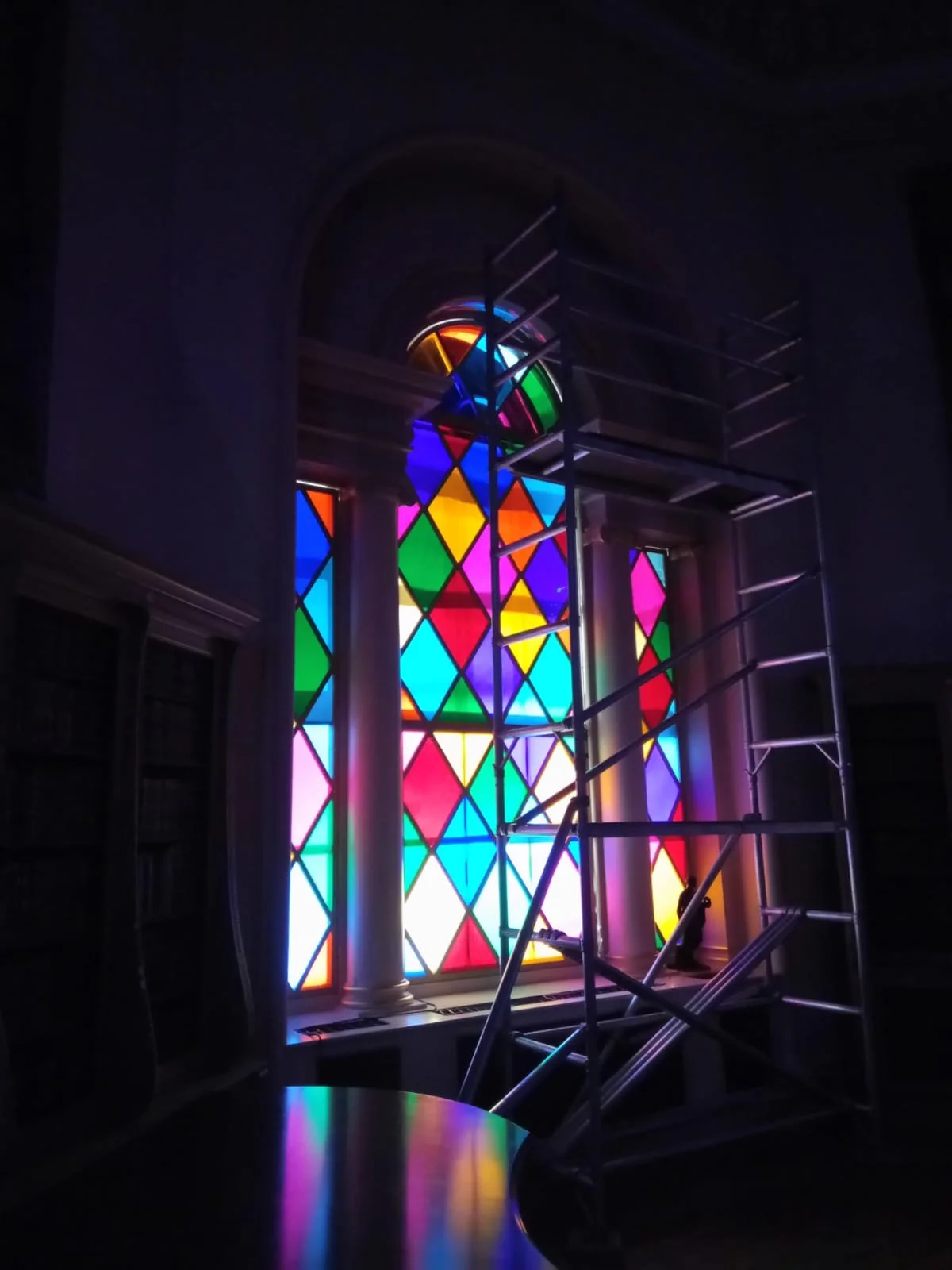 Colorful stained glass window with scaffolding and columns inside a building.