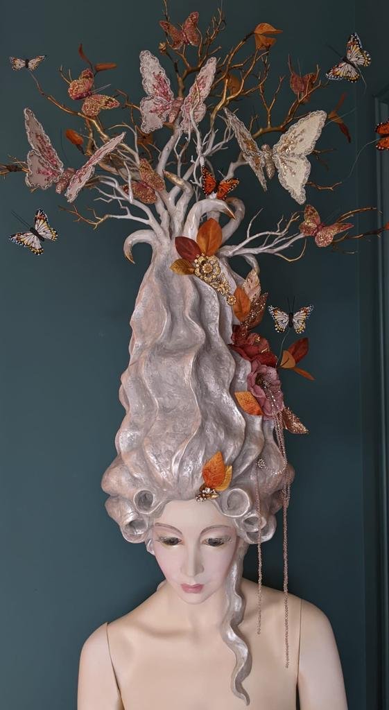 A mannequin with an elaborate headpiece resembling a tree with branches, leaves, and butterflies.
