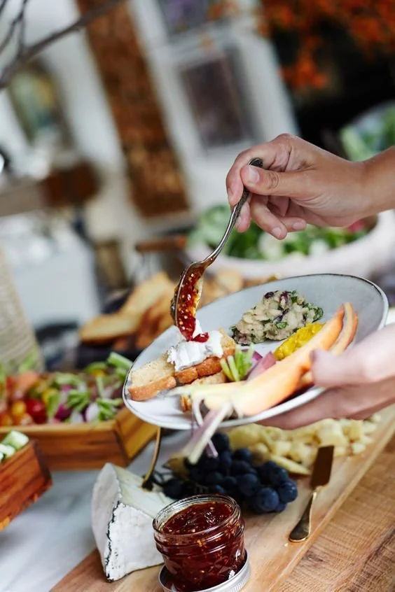 buffet of food with a person holding a plate of fresh food with red sauce on the spoon