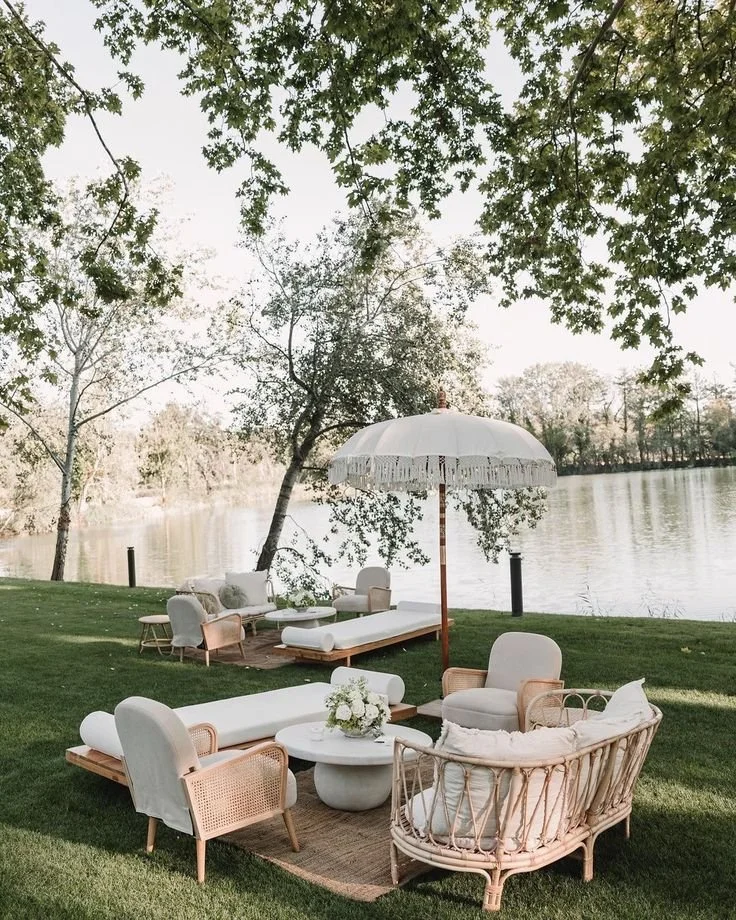 Outdoor patio furniture set with a round table, rattan and cushioned chairs, a large umbrella, a couch, and a view of a river and trees.
