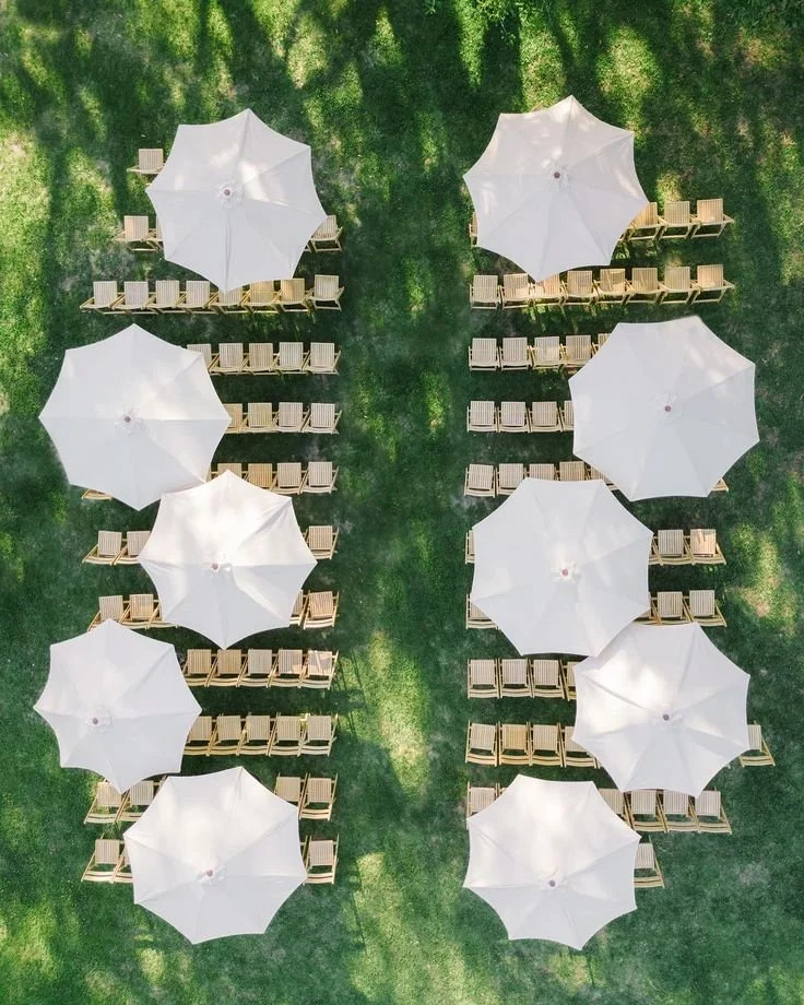 Aerial view of outdoor seating with ten beige lounge chairs and ten white umbrellas on a grassy area.