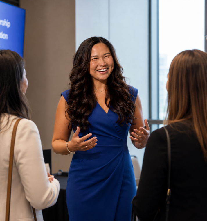 A woman in a blue dress speaking and smiling to a group of three women in a professional setting.