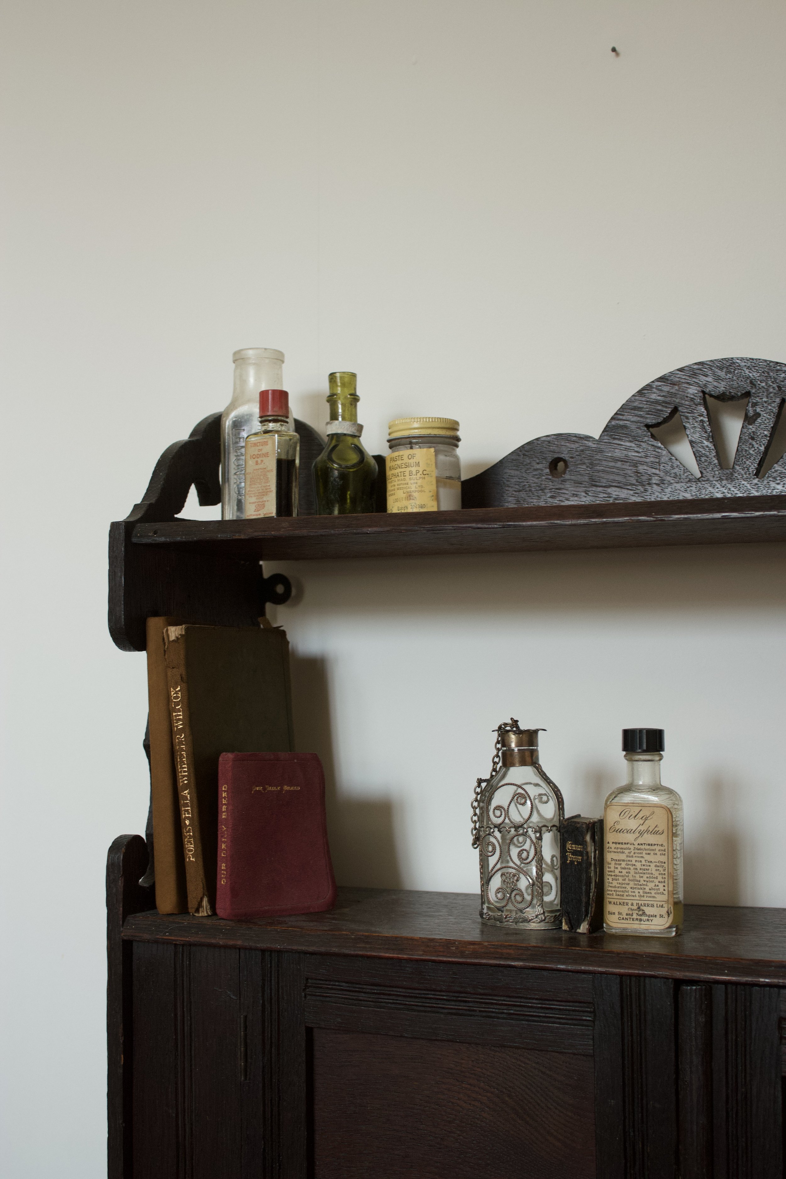 Vintage glass bottles and antique books styled on a wooden shelf in a timeless interior.