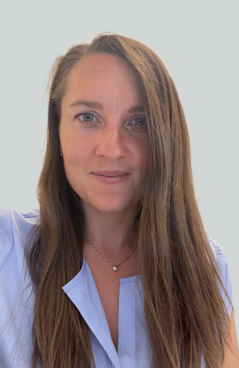 Portrait of a woman with long brown hair, blue eyes, wearing a light blue shirt and a delicate necklace, against a light background.