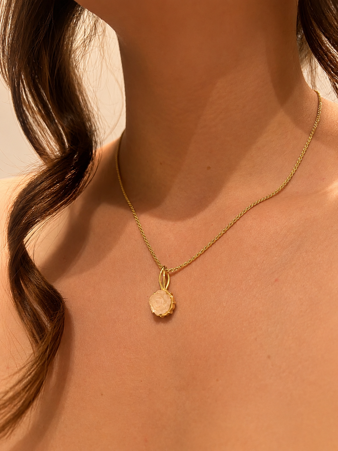 Eine Frau trägt eine goldene Halskette mit einem Anhänger, der eine weiße Rose zeigt.