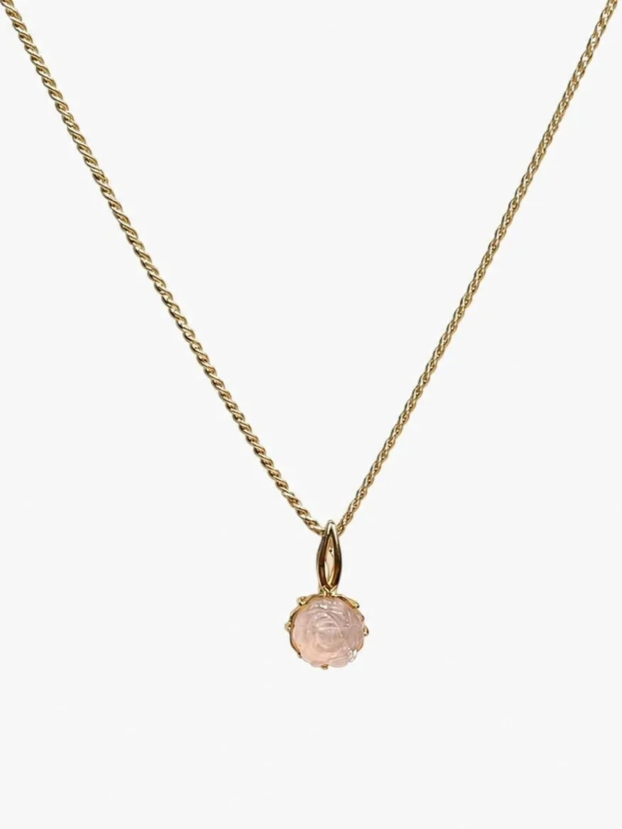 Goldene Halskette mit einem rosa Anhänger in Kreuzform.