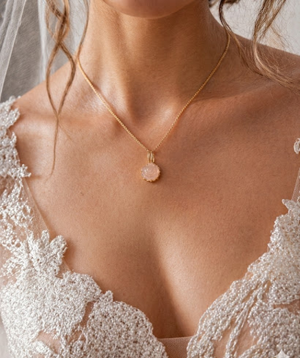 Nackte Haut mit einer goldenen Halskette und einem pinken Anhänger, weiße Spitze am Kleid.