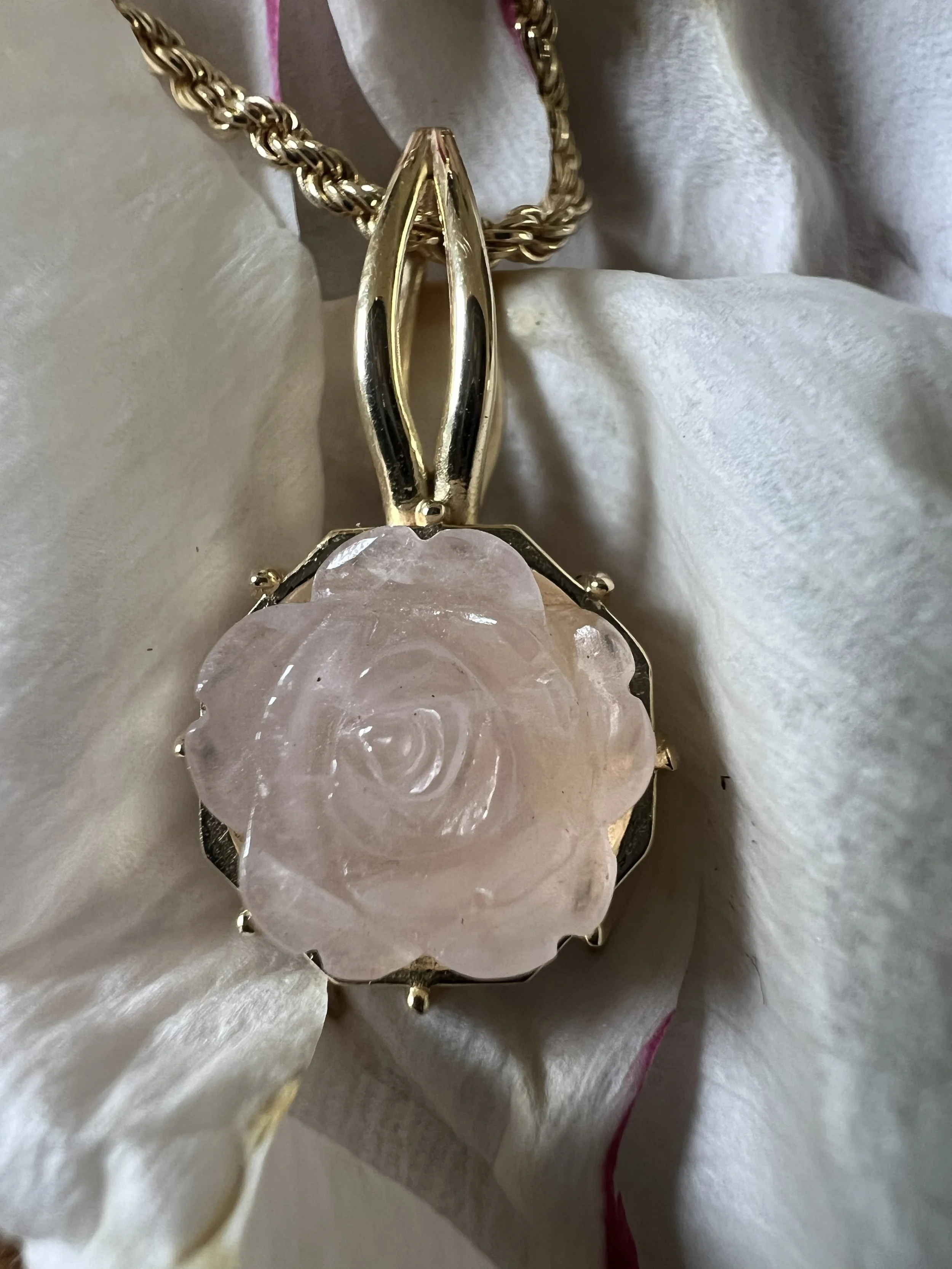 Goldene Halskette mit Anhänger aus rosa Quarz auf weißen Stoff.