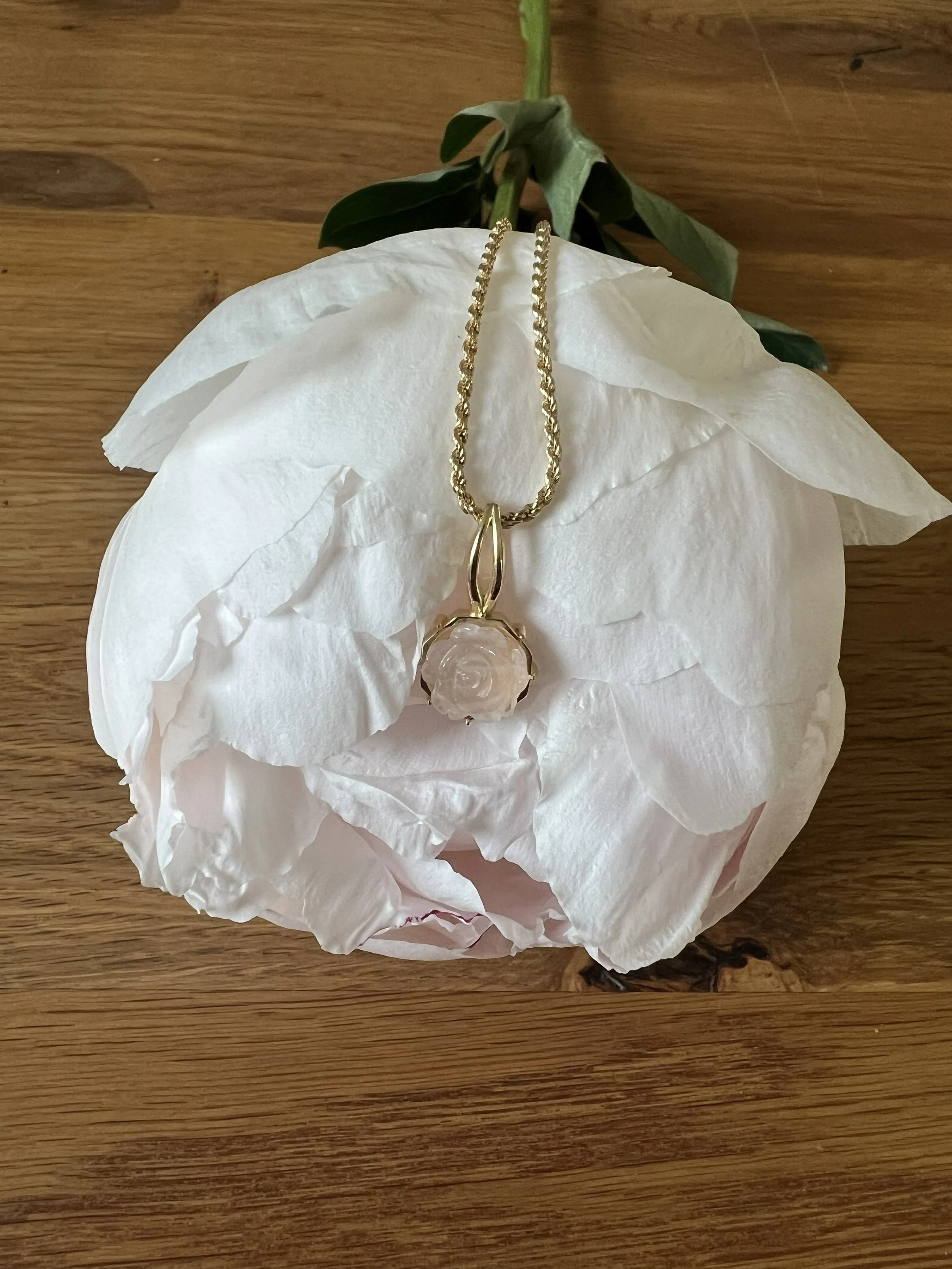 Goldene Halskette mit Anhänger auf weißem Papier und grünem Blatt, auf Holztisch