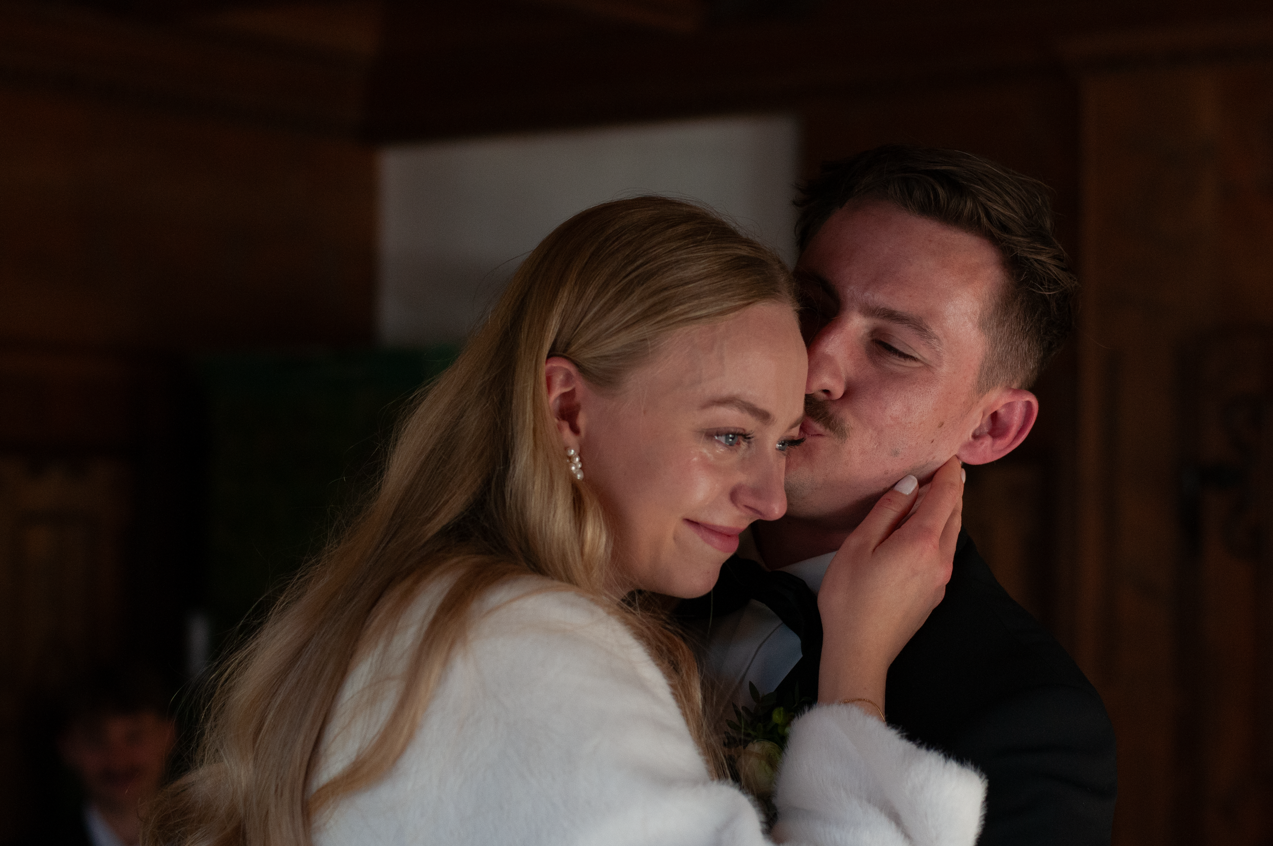 Ein Paar bei einer intimen Umarmung, vermutlich bei einer Hochzeit, die Frauen trägt einen weißen Mantel und der Mann trägt einen schwarzen Anzug.