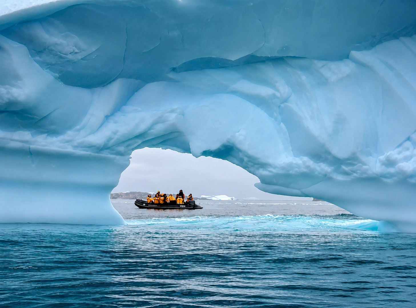 A group of people in orange life jackets on a small boat near a large iceberg in icy waters.
