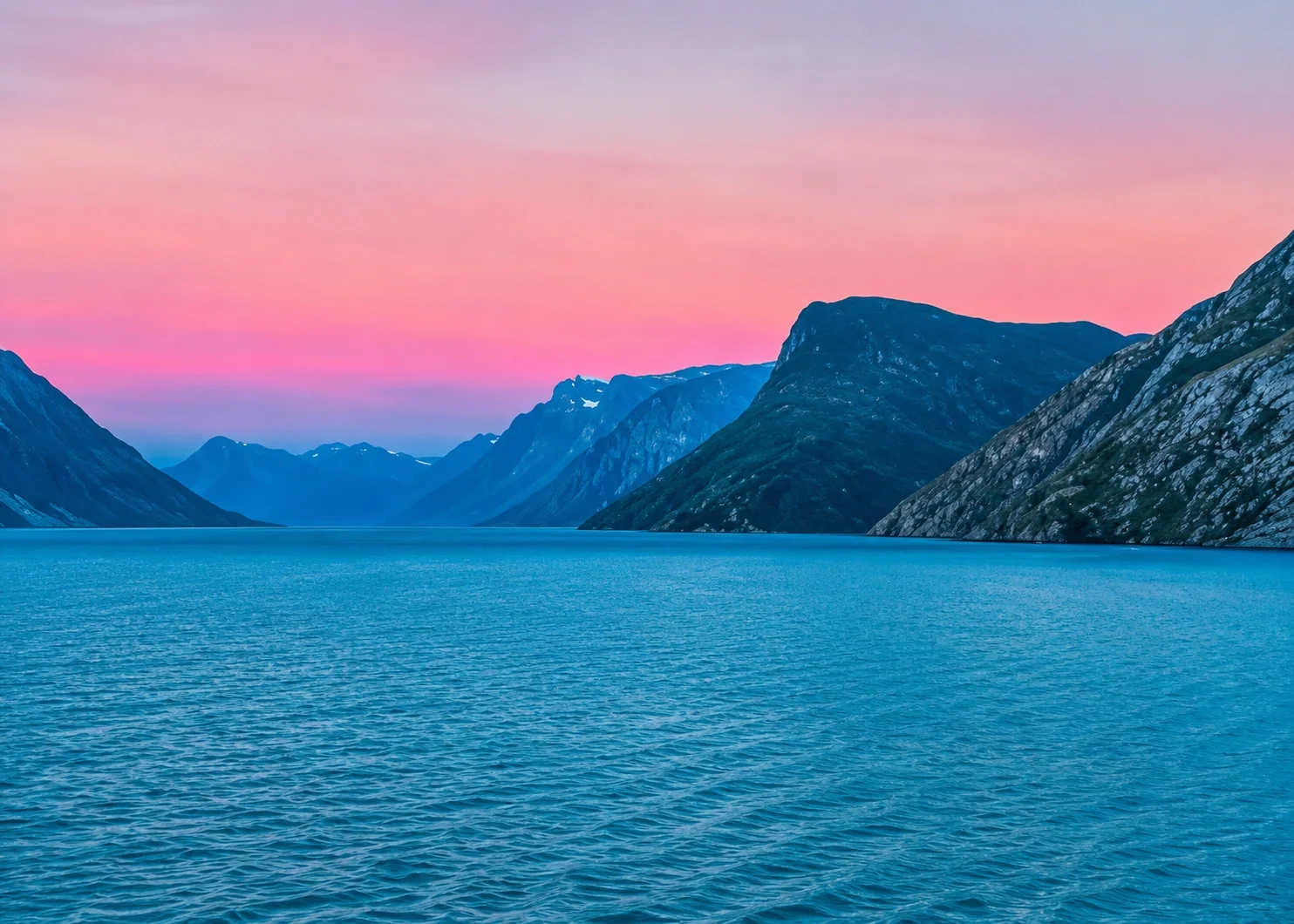 Scenic view of a fjord with blue waters, surrounded by steep mountains, under a pink and purple sunset sky.