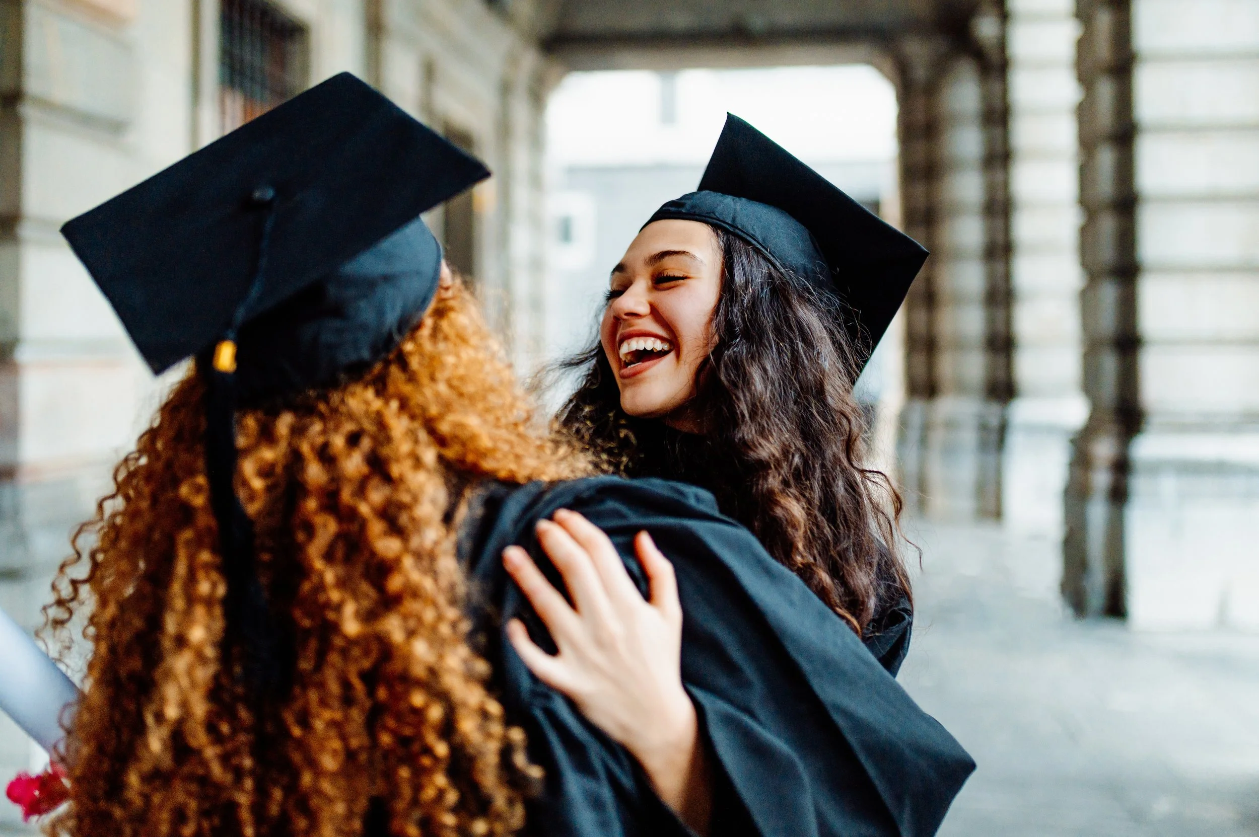 Two students embracing in graduation caps and gowns, celebrating college acceptance and the end of the admissions process