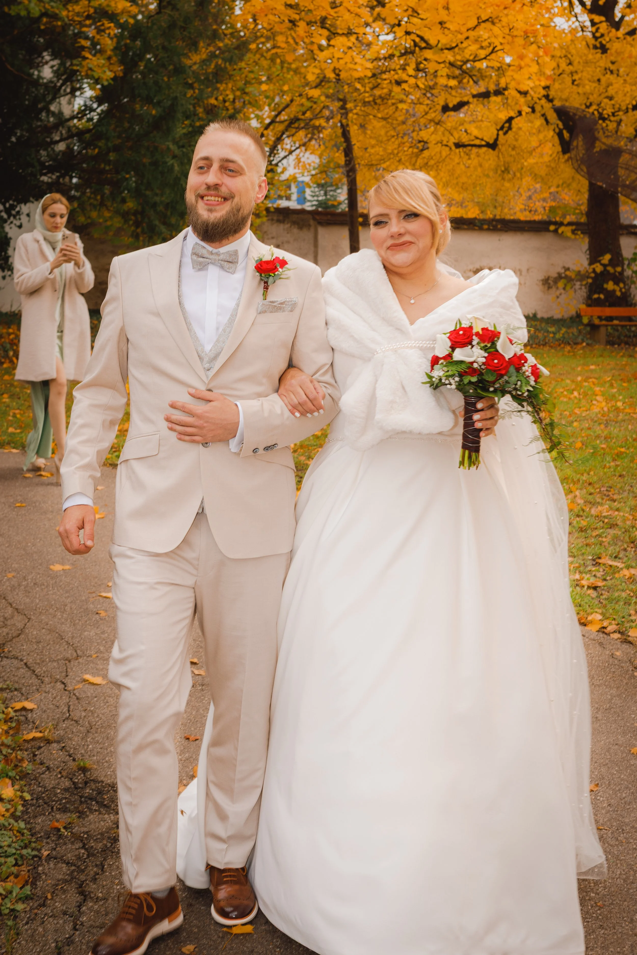 Brautpaar geht Hand in Hand durch einen herbstlichen Park mit goldenem Laub