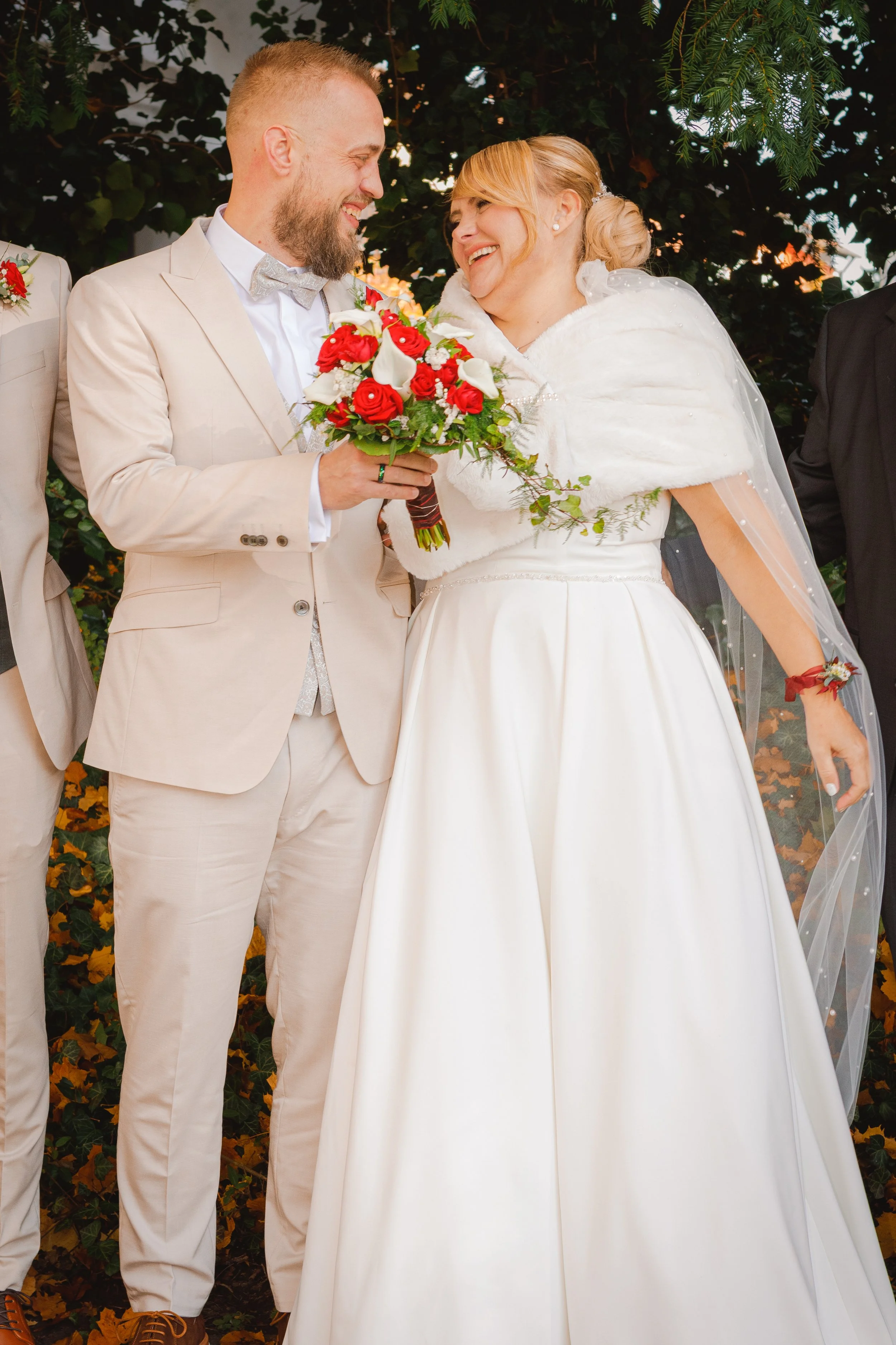 Brautpaar steht eng beieinander, die Braut hält einen Strauß aus roten Rosen