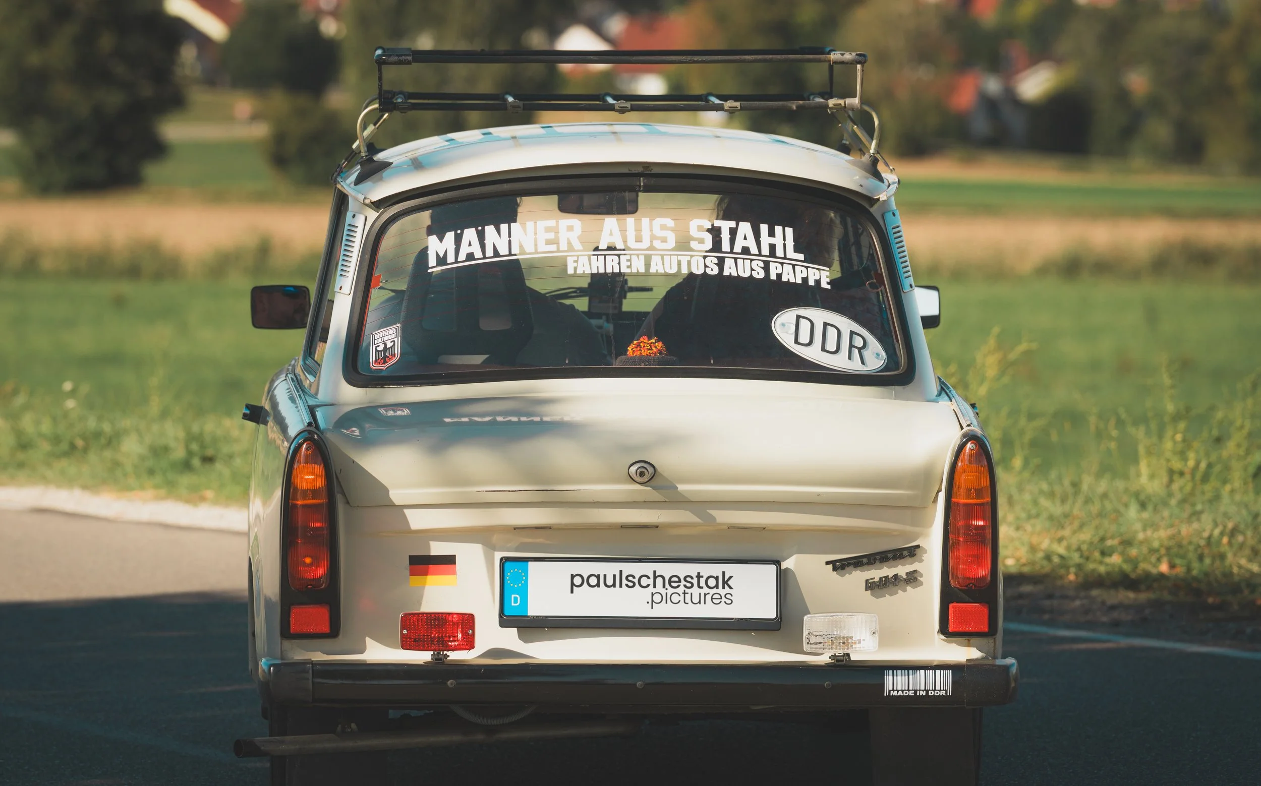Beiger Trabant 601 mit Dachgepäckträger und DDR-Aufkleber von hinten